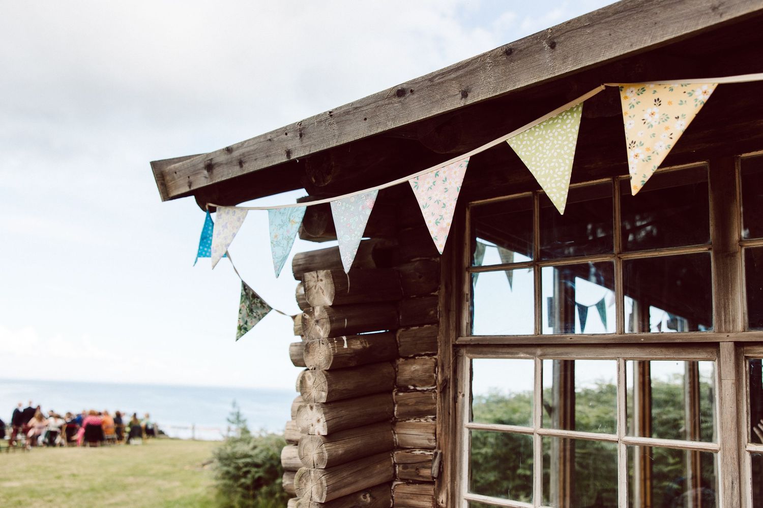 Rustic wooden beach house with white bunting flags decorating the porch and ocean views in the background.