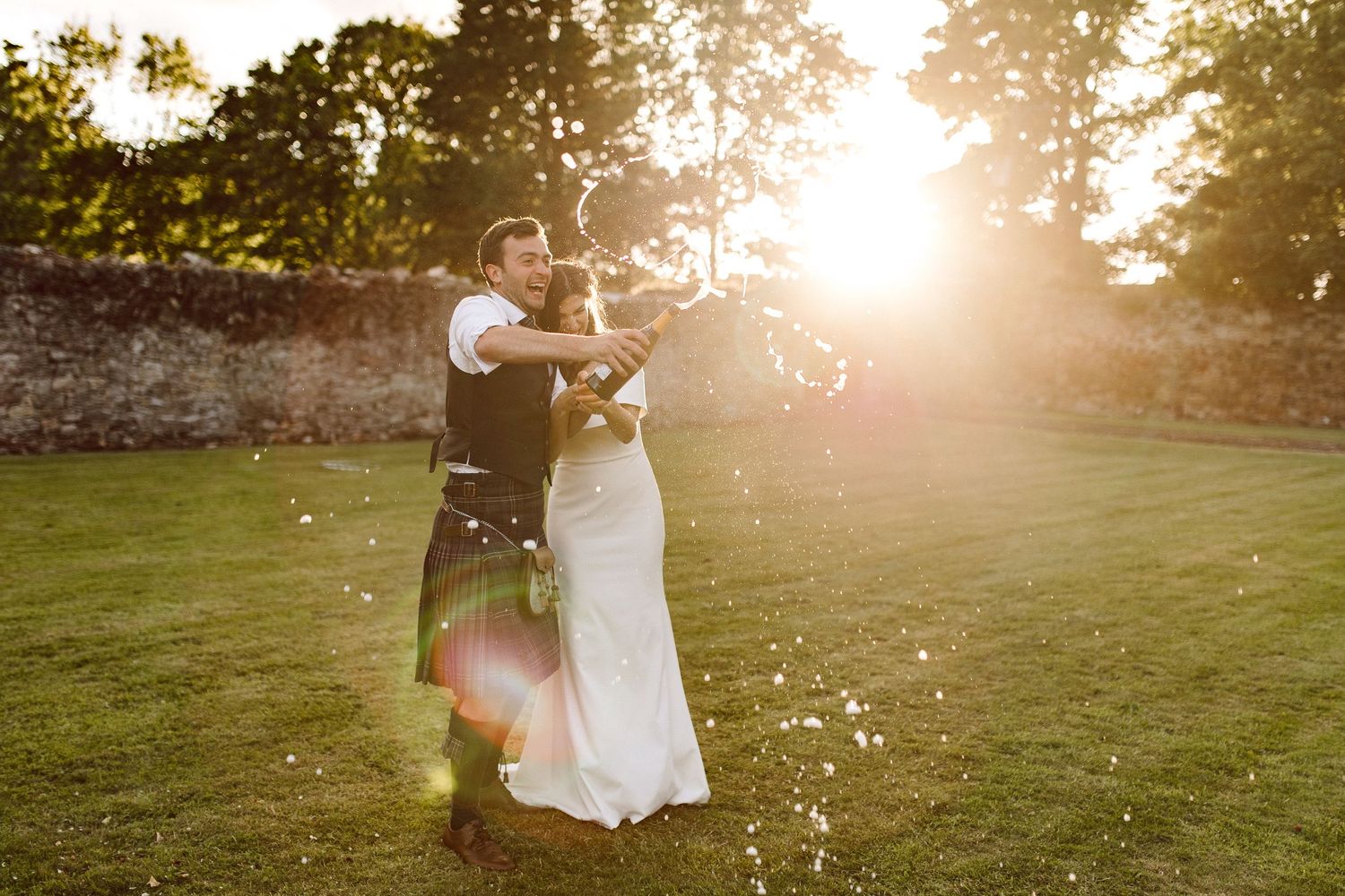 Romantic silhouette of newlyweds embracing in golden sunlight during sunset at outdoor wedding ceremony.