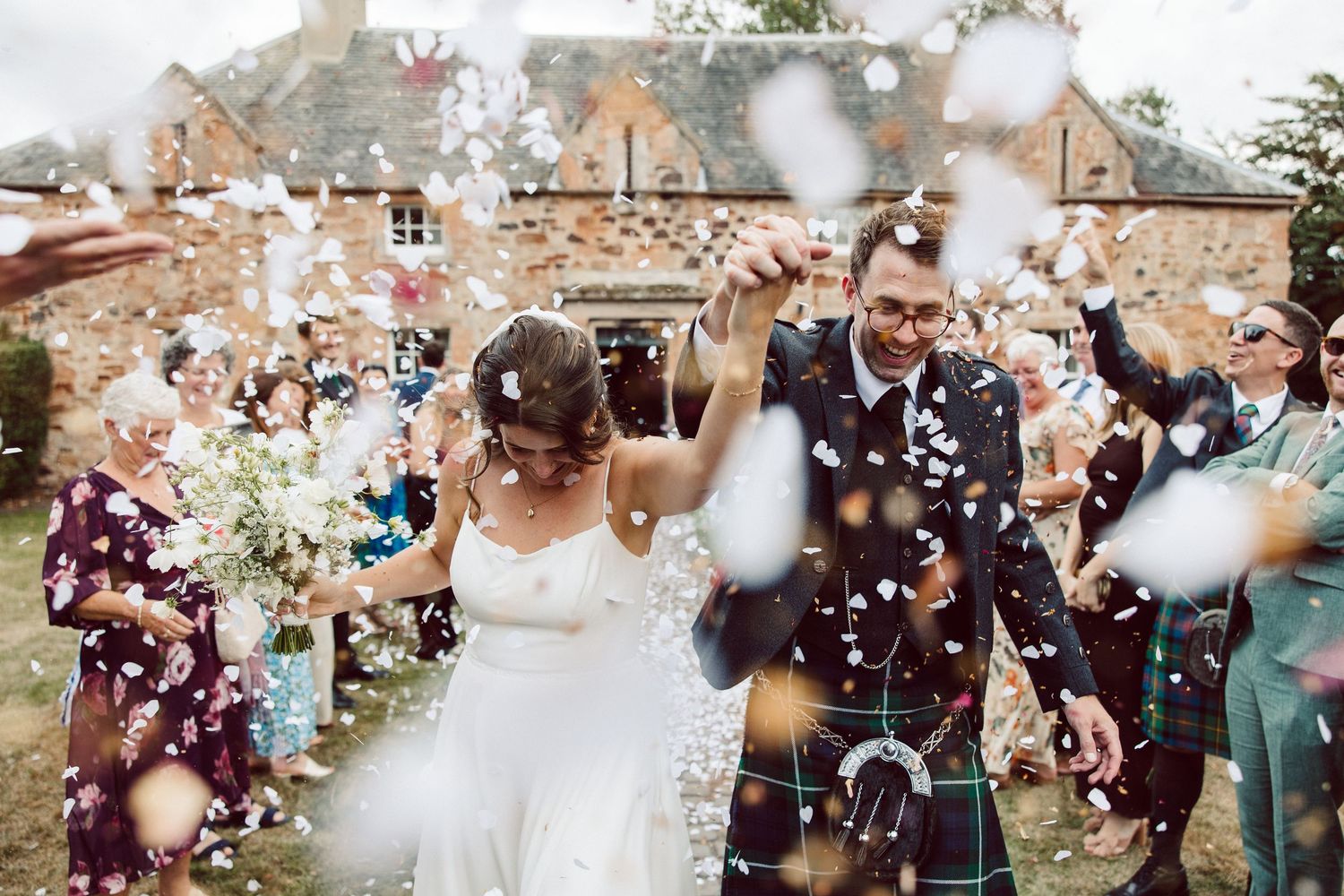 Wedding celebration with confetti being thrown over couple during outdoor ceremony at rustic venue.