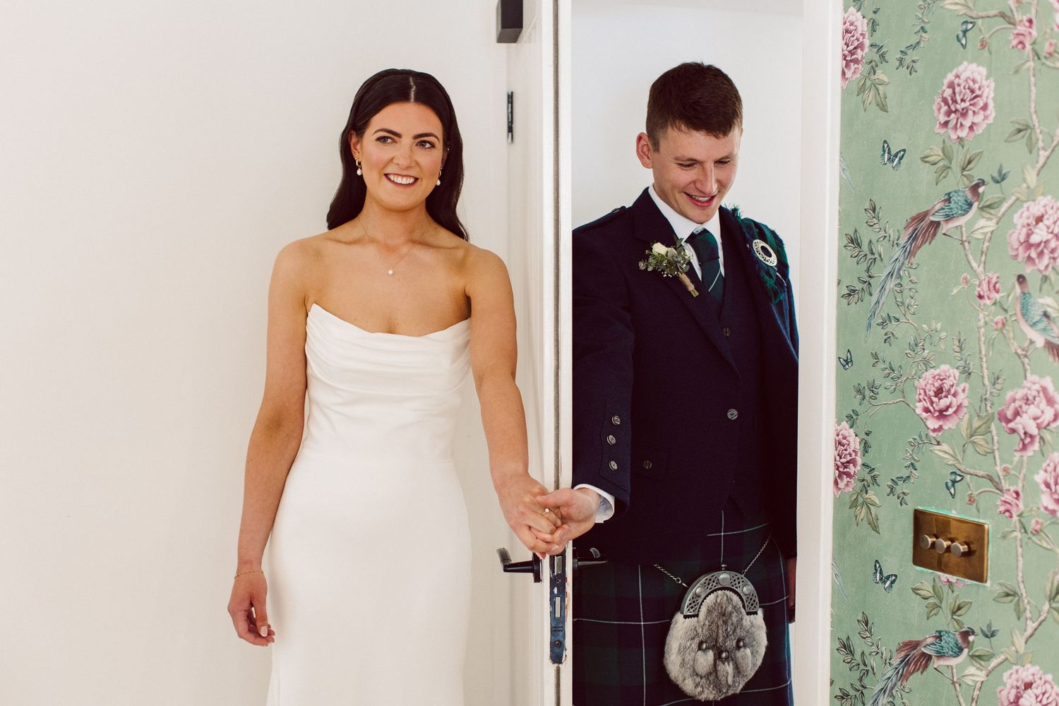 A bride and groom share a romantic moment against a floral wallpaper backdrop during their wedding day.