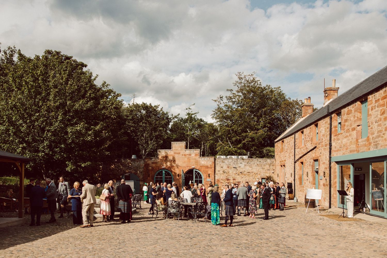 A crowd of people gather in a cobblestone courtyard surrounded by historic brick buildings on a cloudy day.