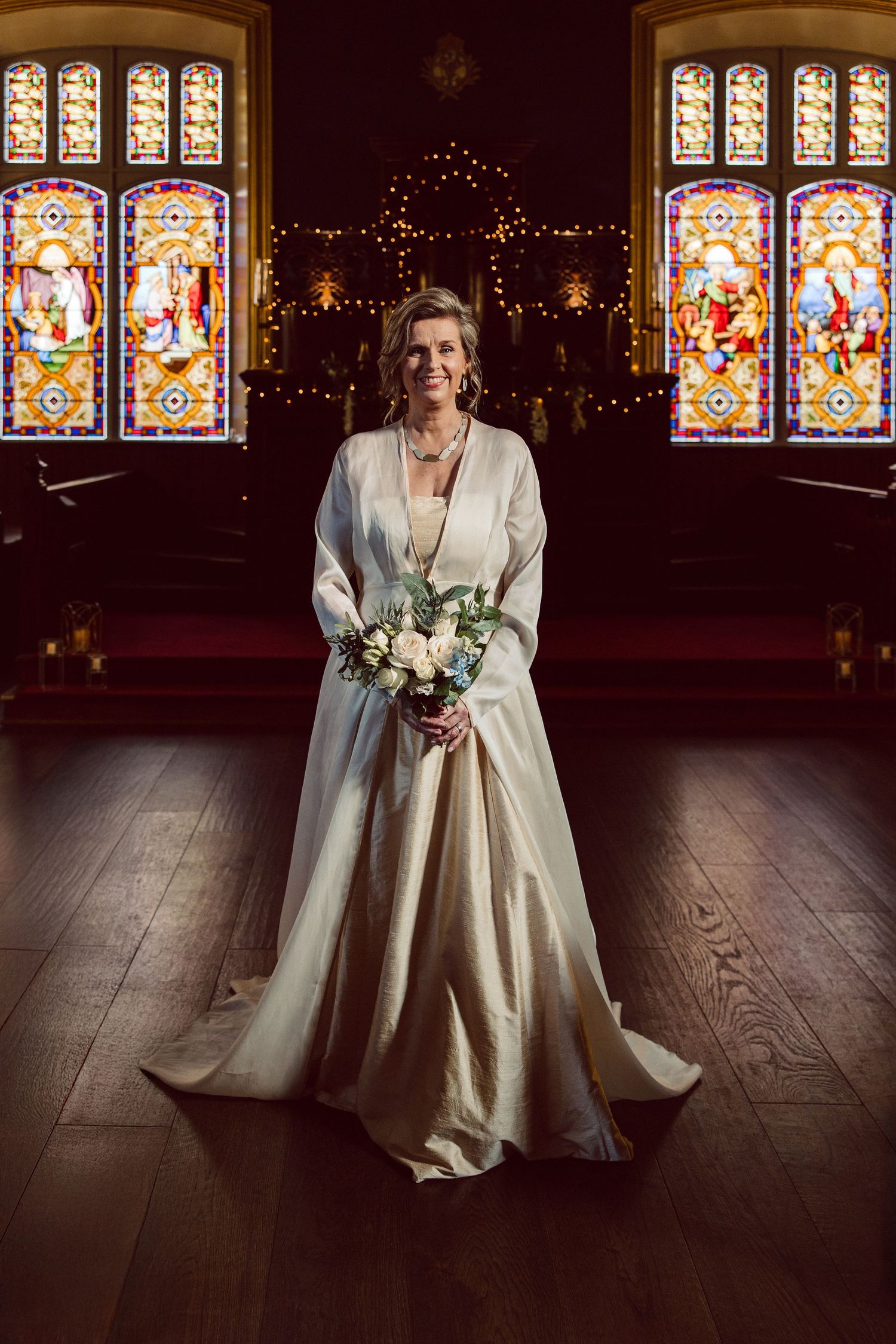 A wedding photo in a church with beautiful stained glass windows and soft lighting illuminating the elegant bridal gown.