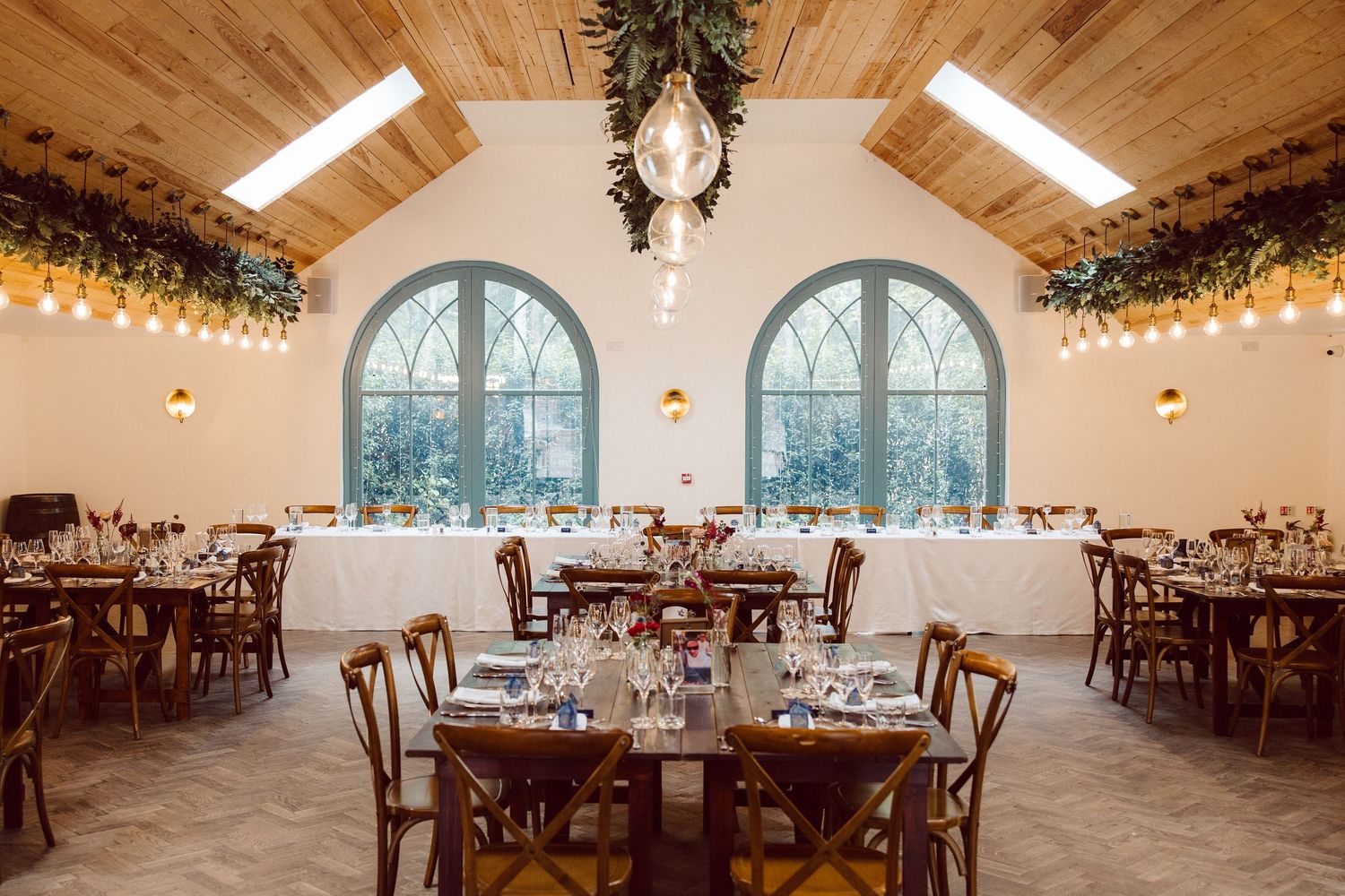 Rustic wedding reception venue with wooden ceiling beams, arched windows, and elegant table settings in natural light.