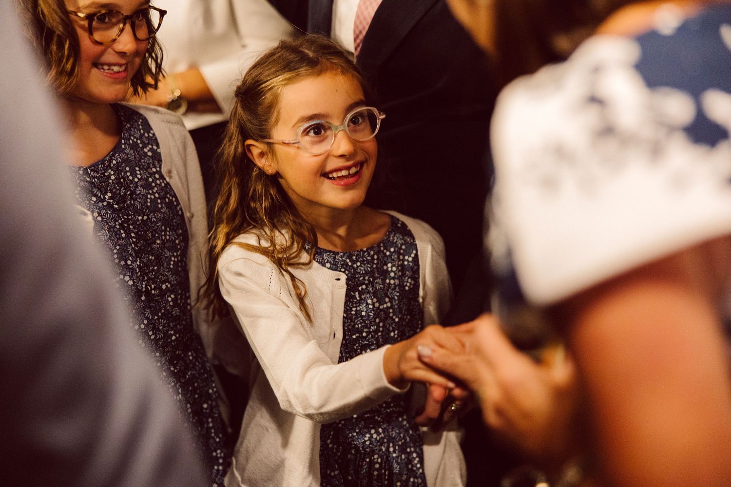 A person in glasses and dark attire smiles while interacting with others at an event.