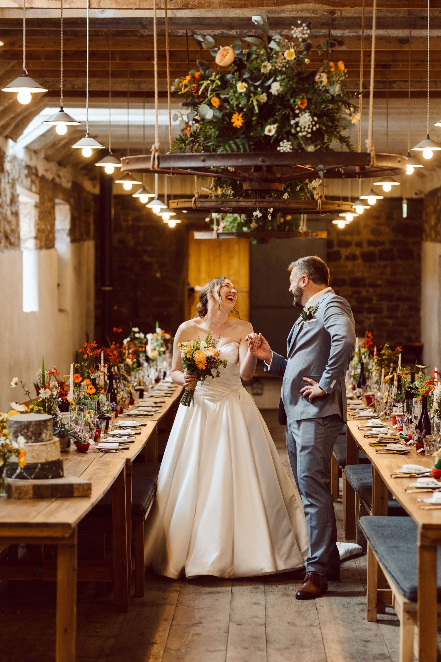 A romantic wedding couple shares an intimate moment in a rustic reception venue with long wooden tables and hanging lights.