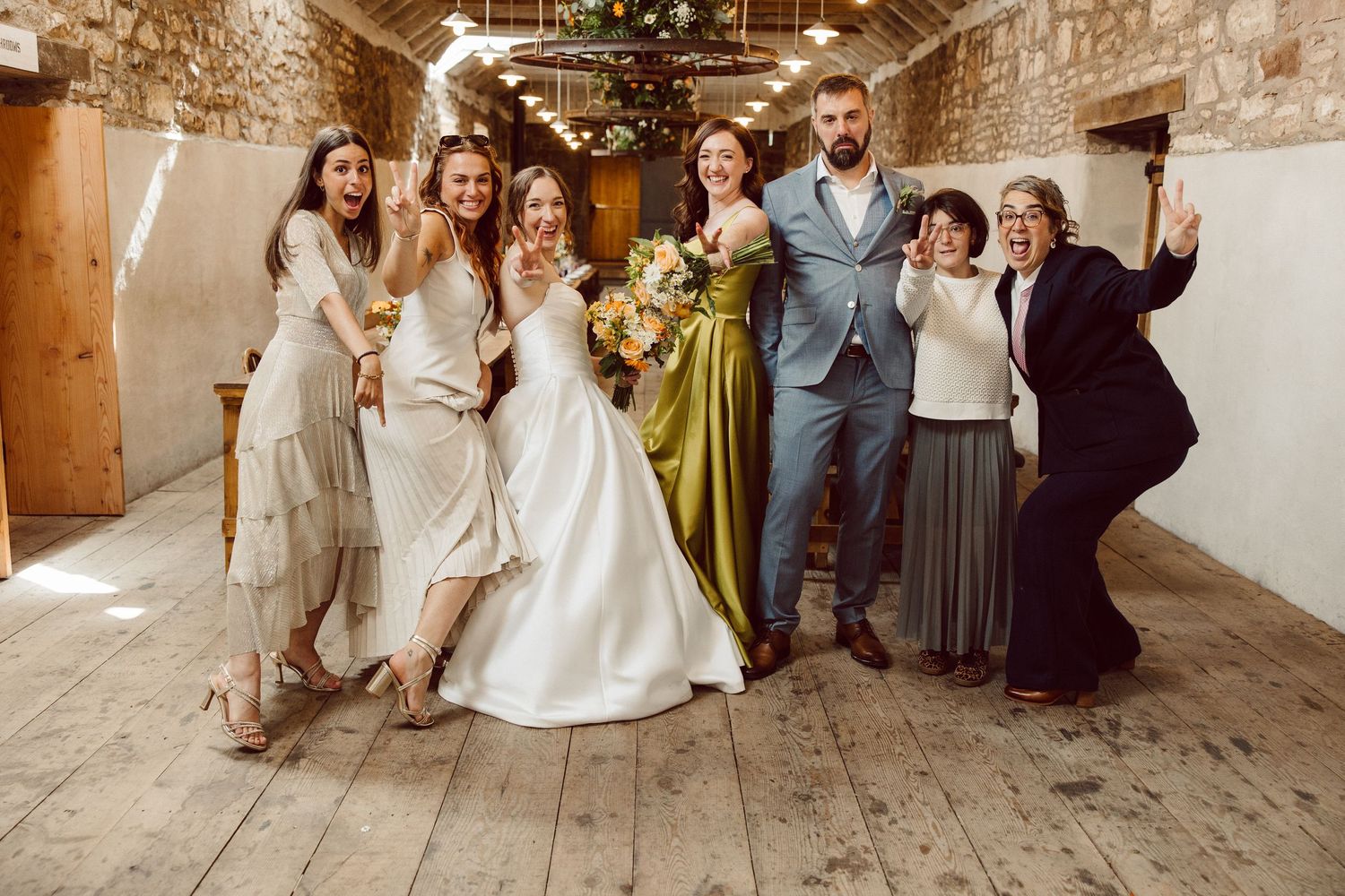 Wedding party celebrates in rustic barn venue with string lights and exposed brick walls.
