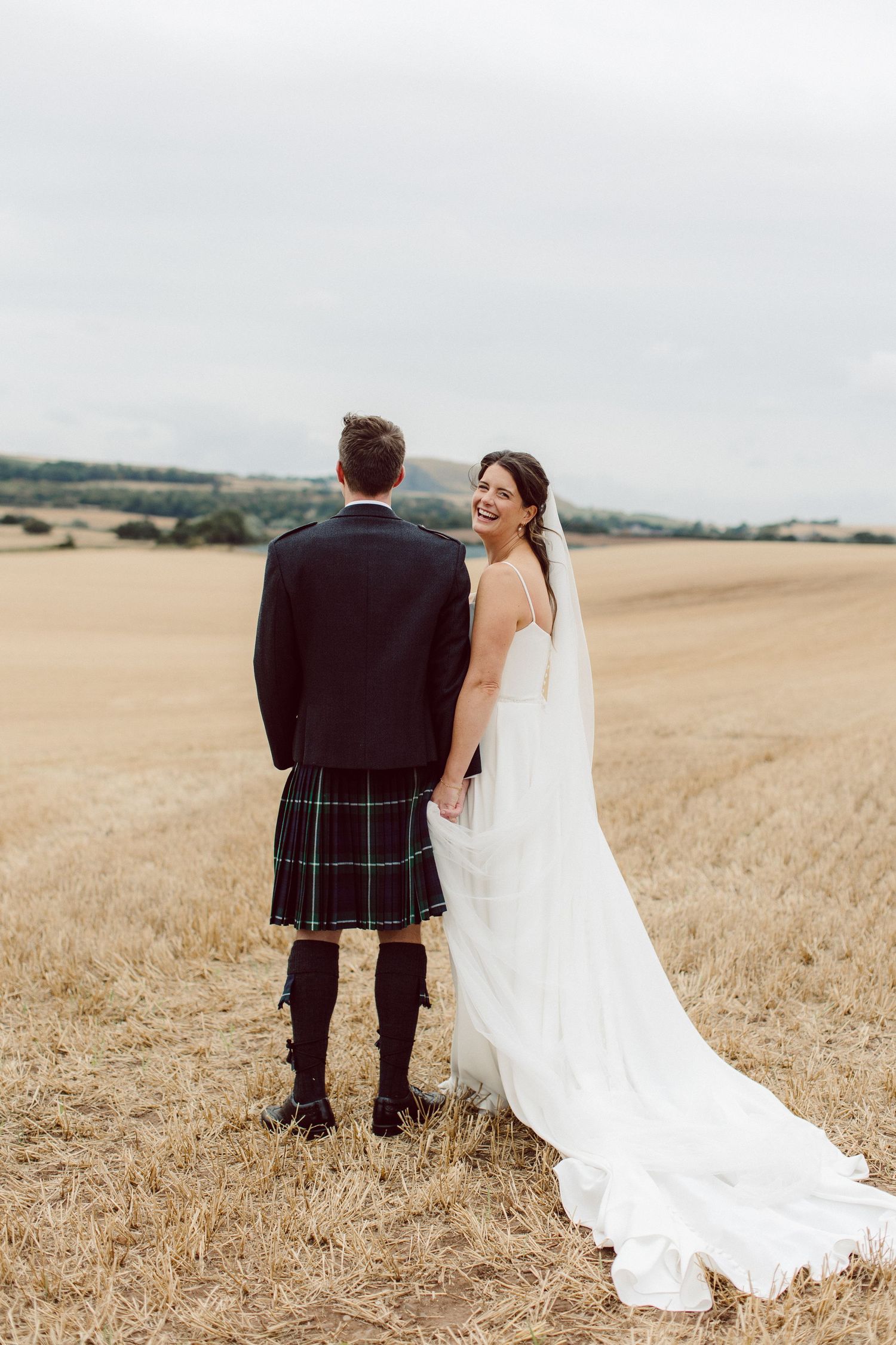 A couple in wedding attire walk through a golden wheat field on their special day.