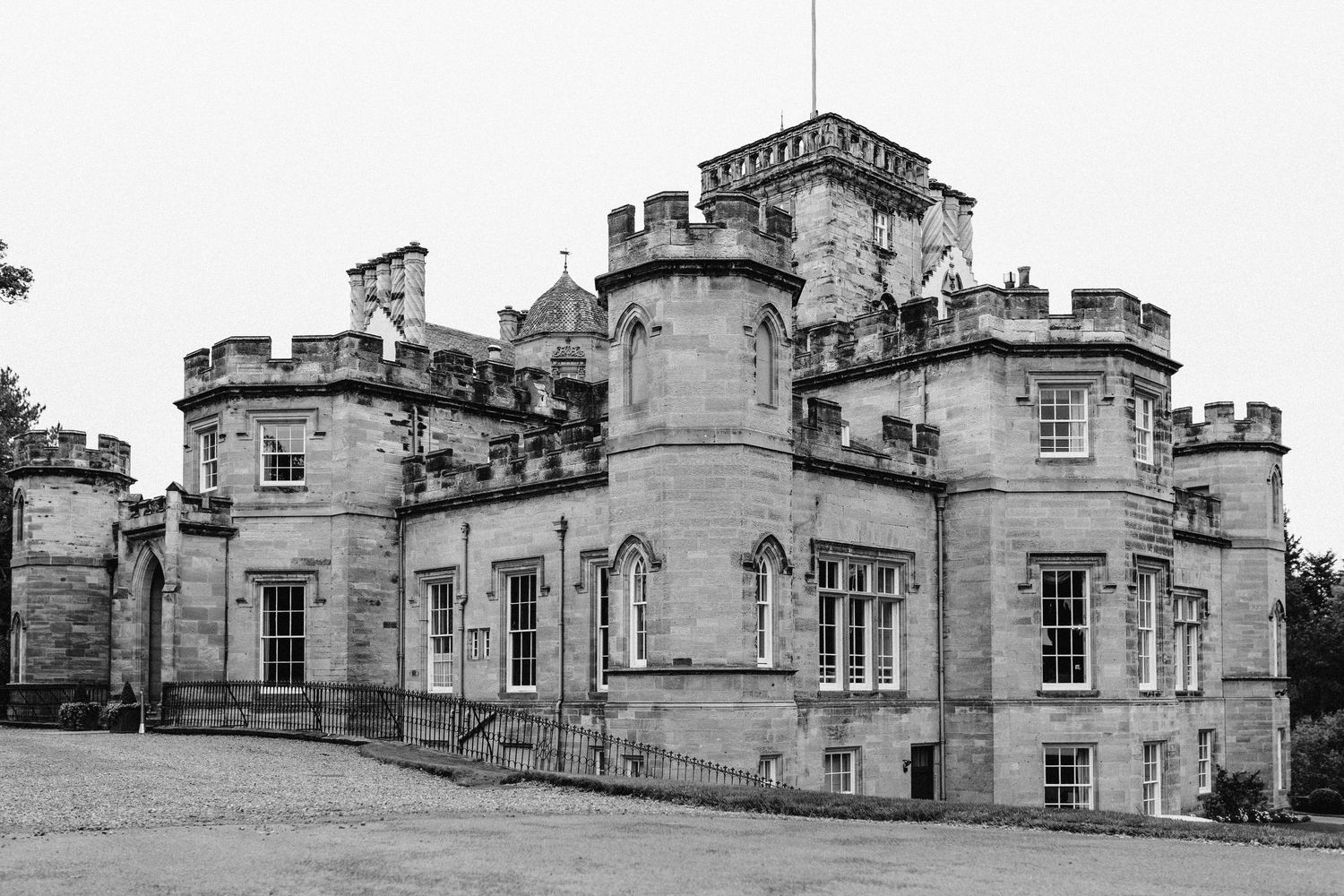 Historic black and white panoramic view of a Scottish castle-style manor with turrets and stone architecture.