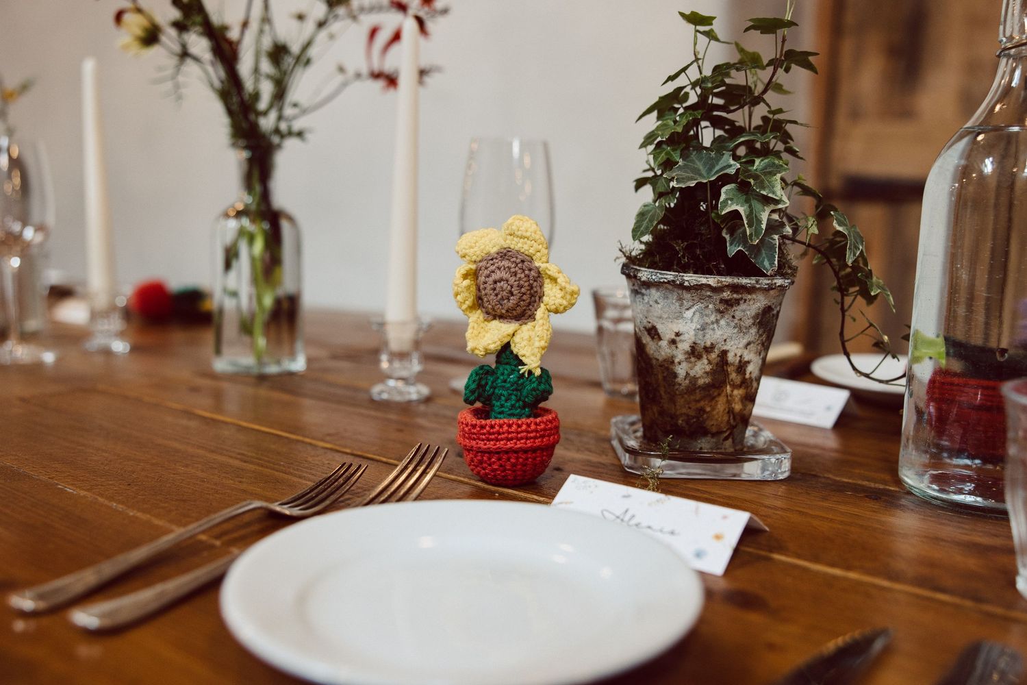A rustic wooden dining table set with elegant glassware and small potted plants as centerpieces.