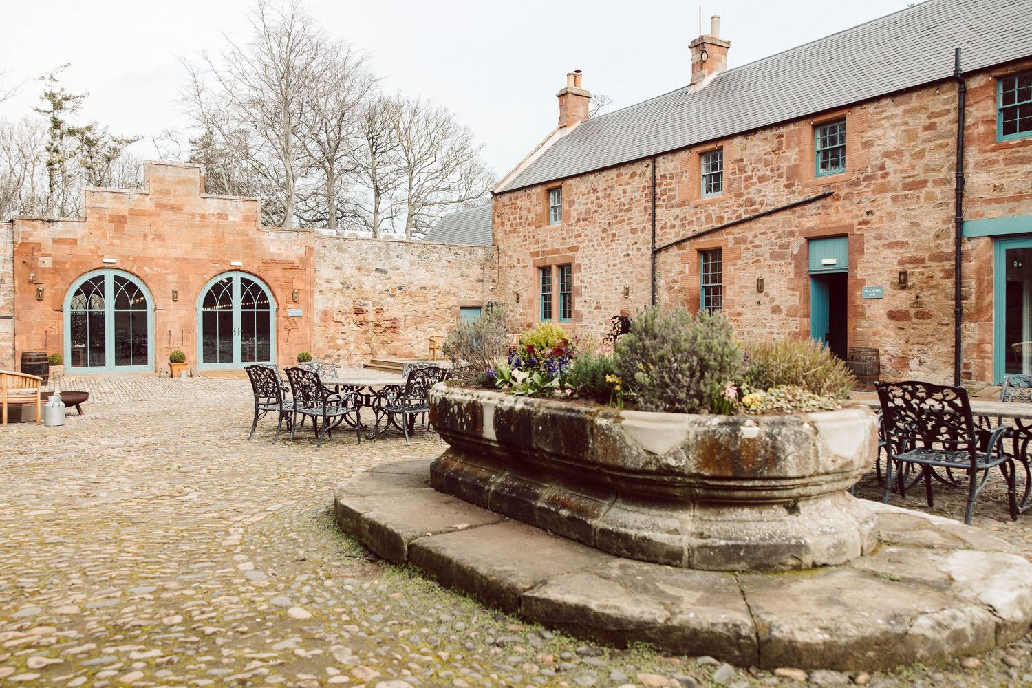Stone patio and seating area with rustic brick buildings and garden walls in a historic courtyard setting.