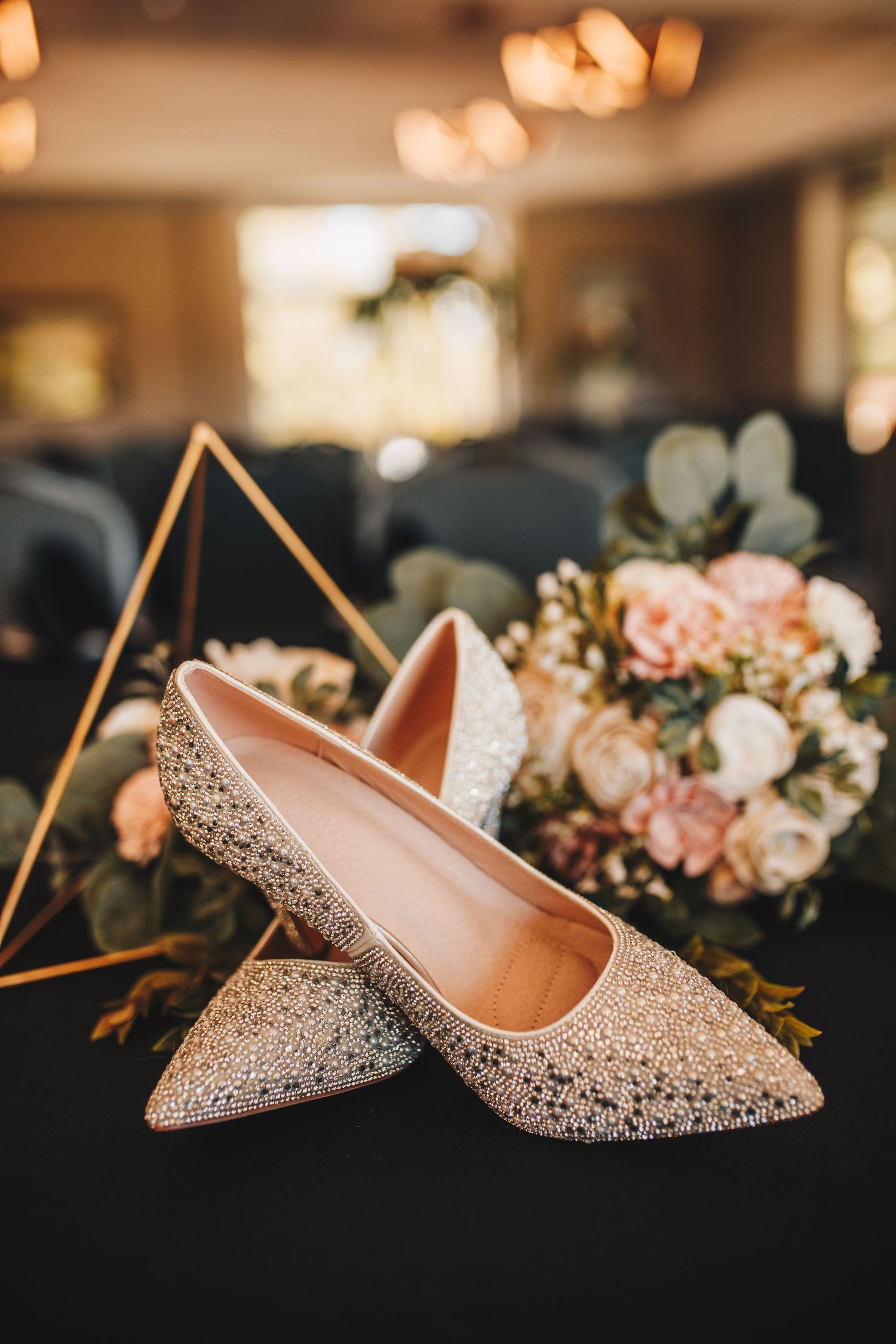Sparkling crystal bridal heels displayed beside a soft pink and white floral bouquet.