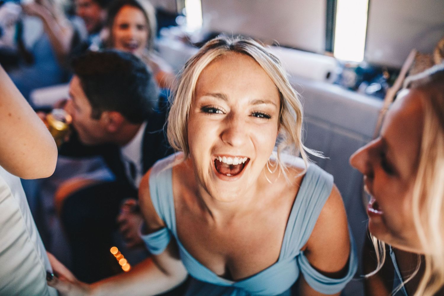 Joyful bridesmaid in light blue dress laughing candidly during wedding celebration on party bus.