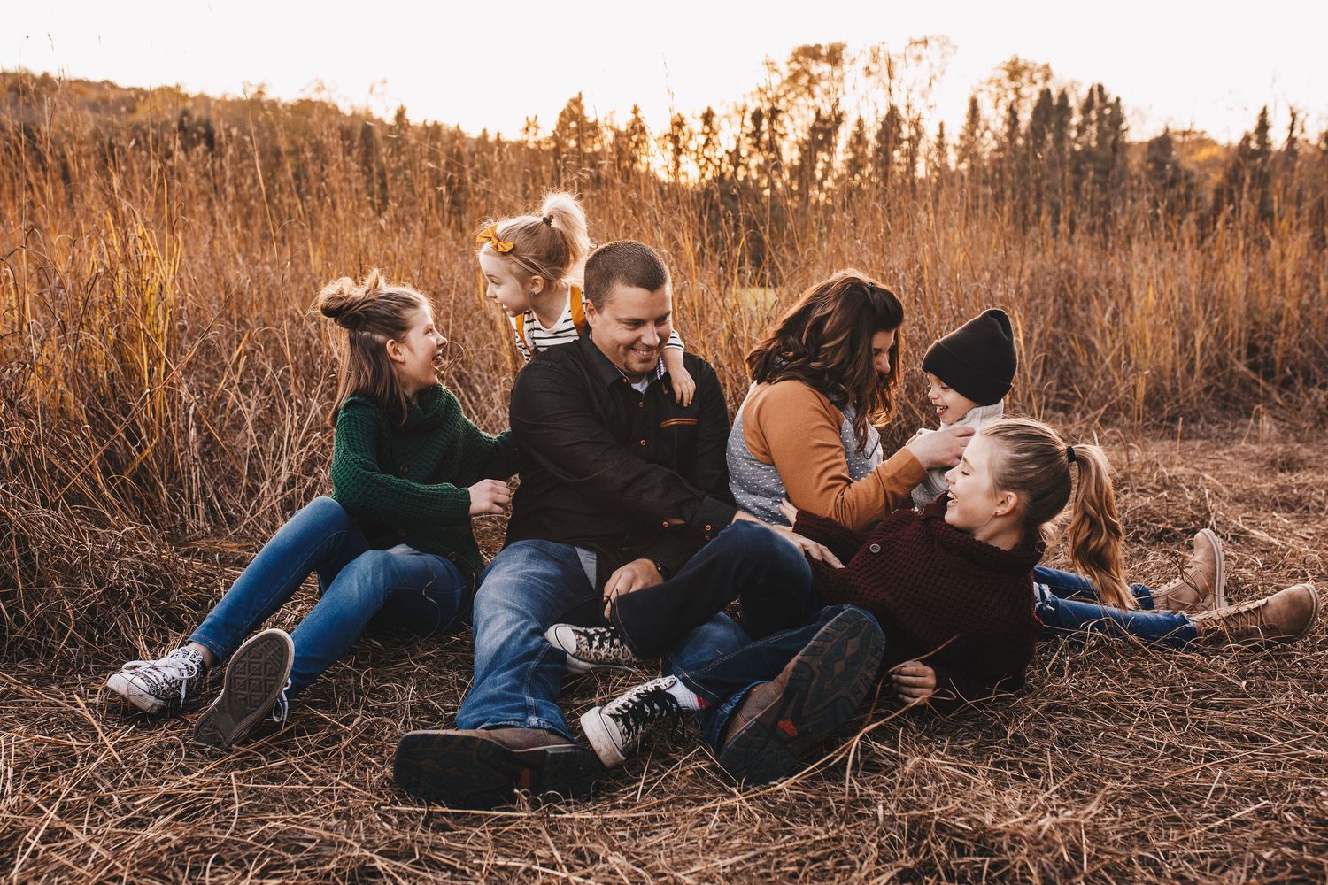 A joyful family laughing together while sitting in a field of golden autumn grass at sunset.