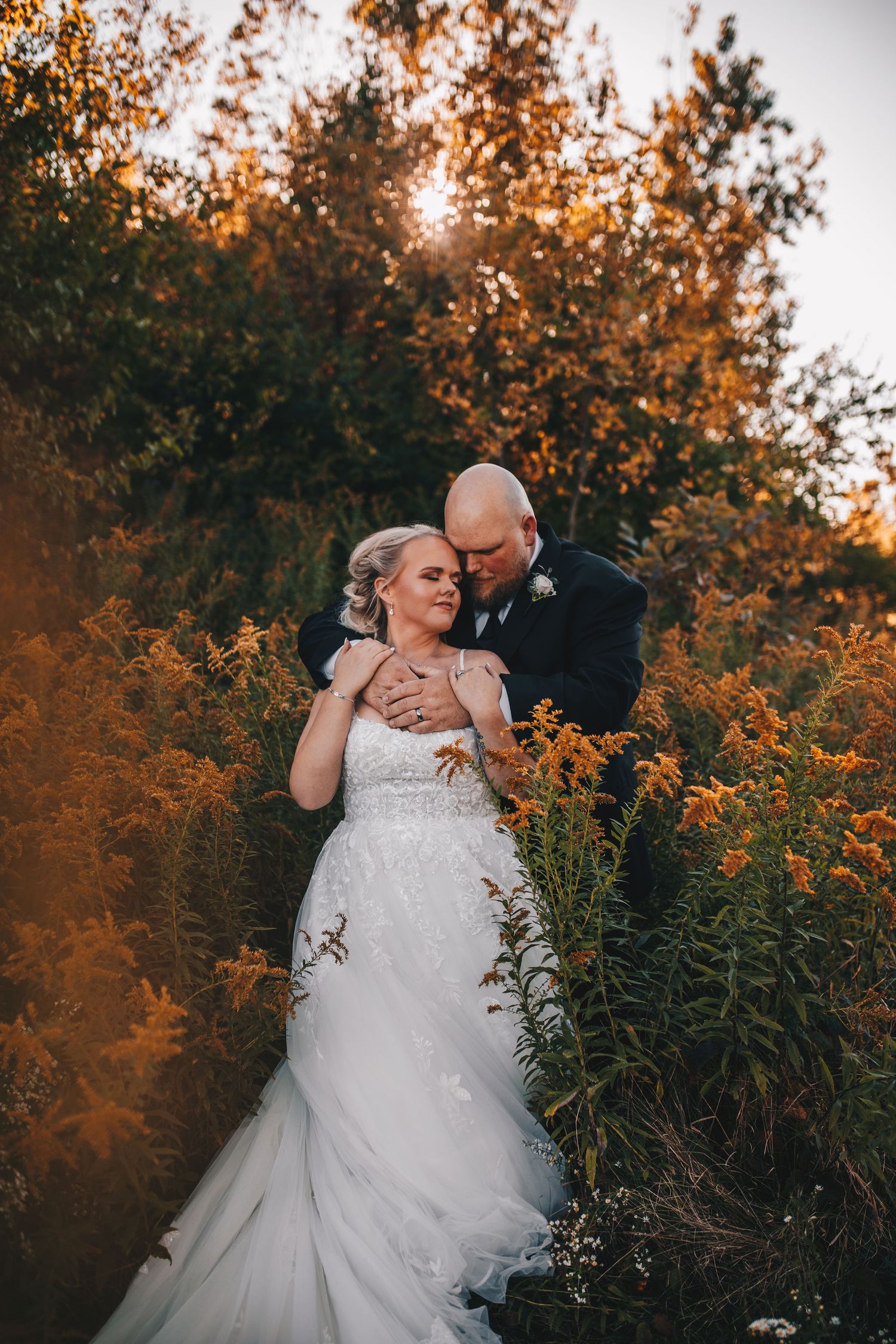 Bride and groom embracing tenderly in vibrant golden autumn foliage at sunset.