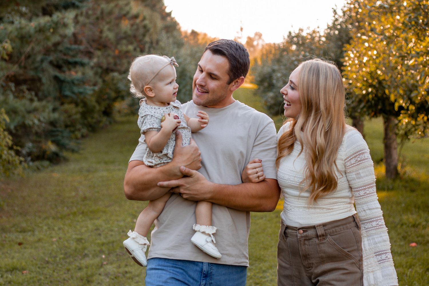 Happy family with baby outdoors in golden hour light among green trees.