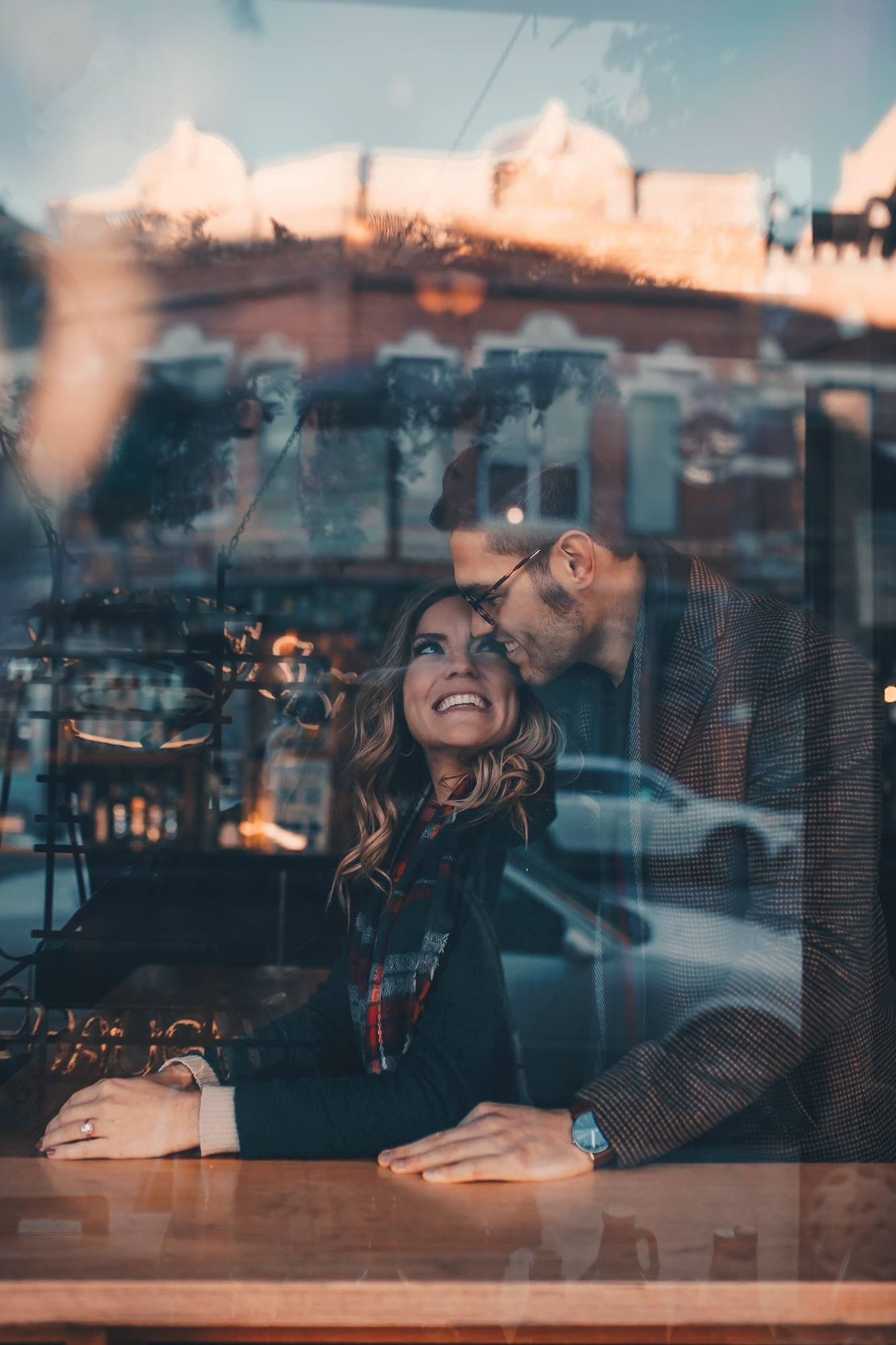 Happy couple sharing romantic moment inside cafe, viewed through window with city street reflections.