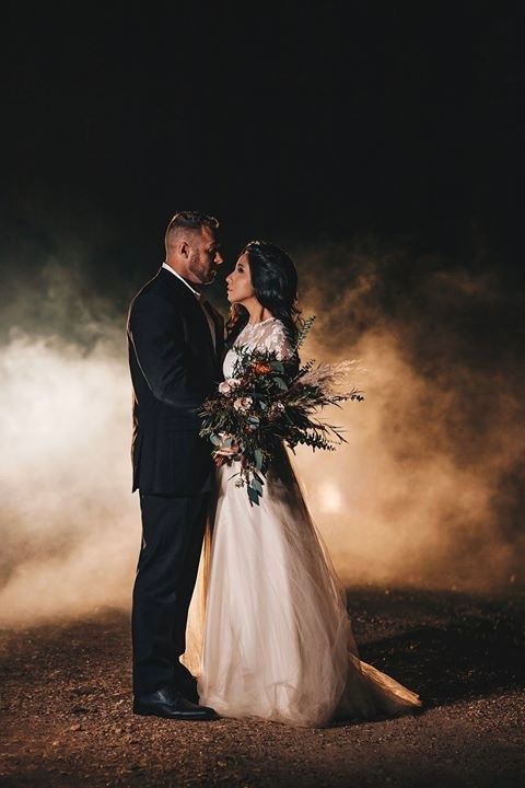 Bride and groom share intimate moment surrounded by dramatic smoke clouds in dark outdoor night setting.