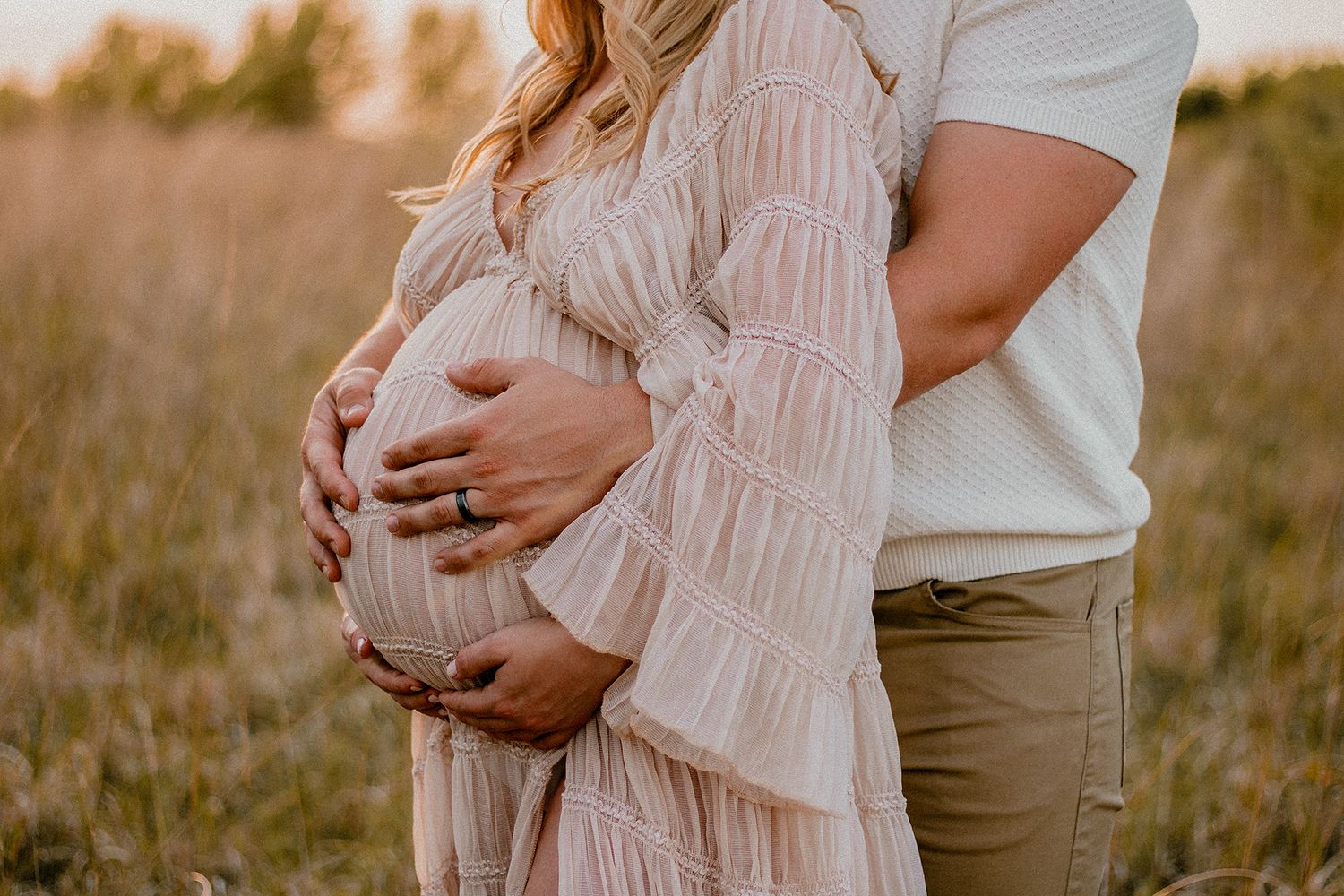 Couple embracing pregnant belly in golden field at sunset, maternity photo.