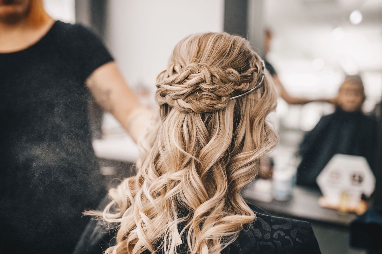 Elegant half-up braided hairstyle with soft curls on blonde bride in salon setting.