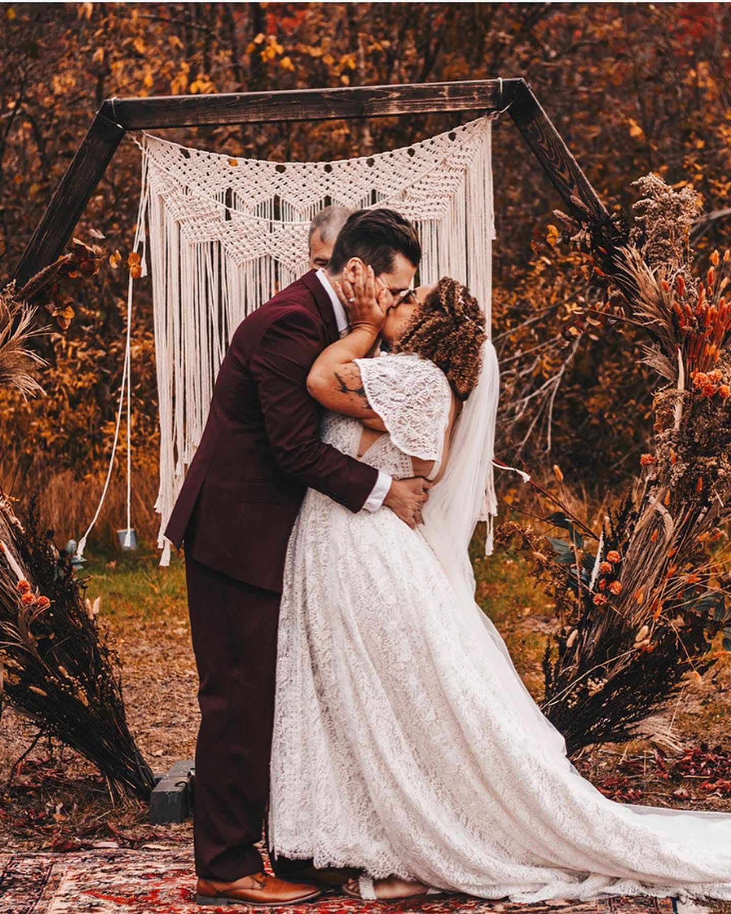 Couple sharing first kiss under boho macrame arch surrounded by rich fall colors.