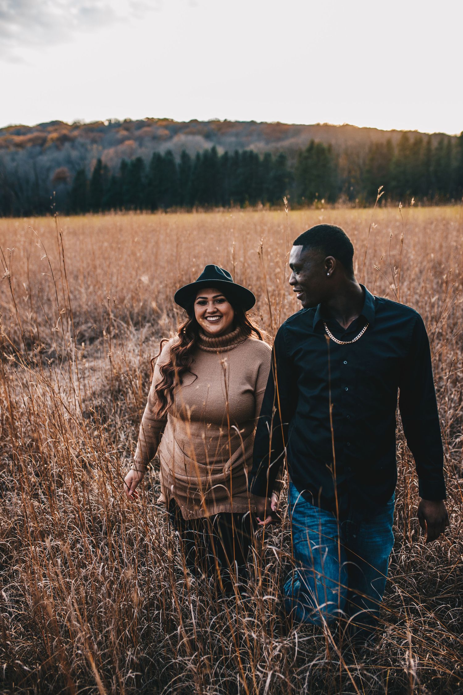 Happy couple walks hand in hand through a dry autumn field at golden hour.