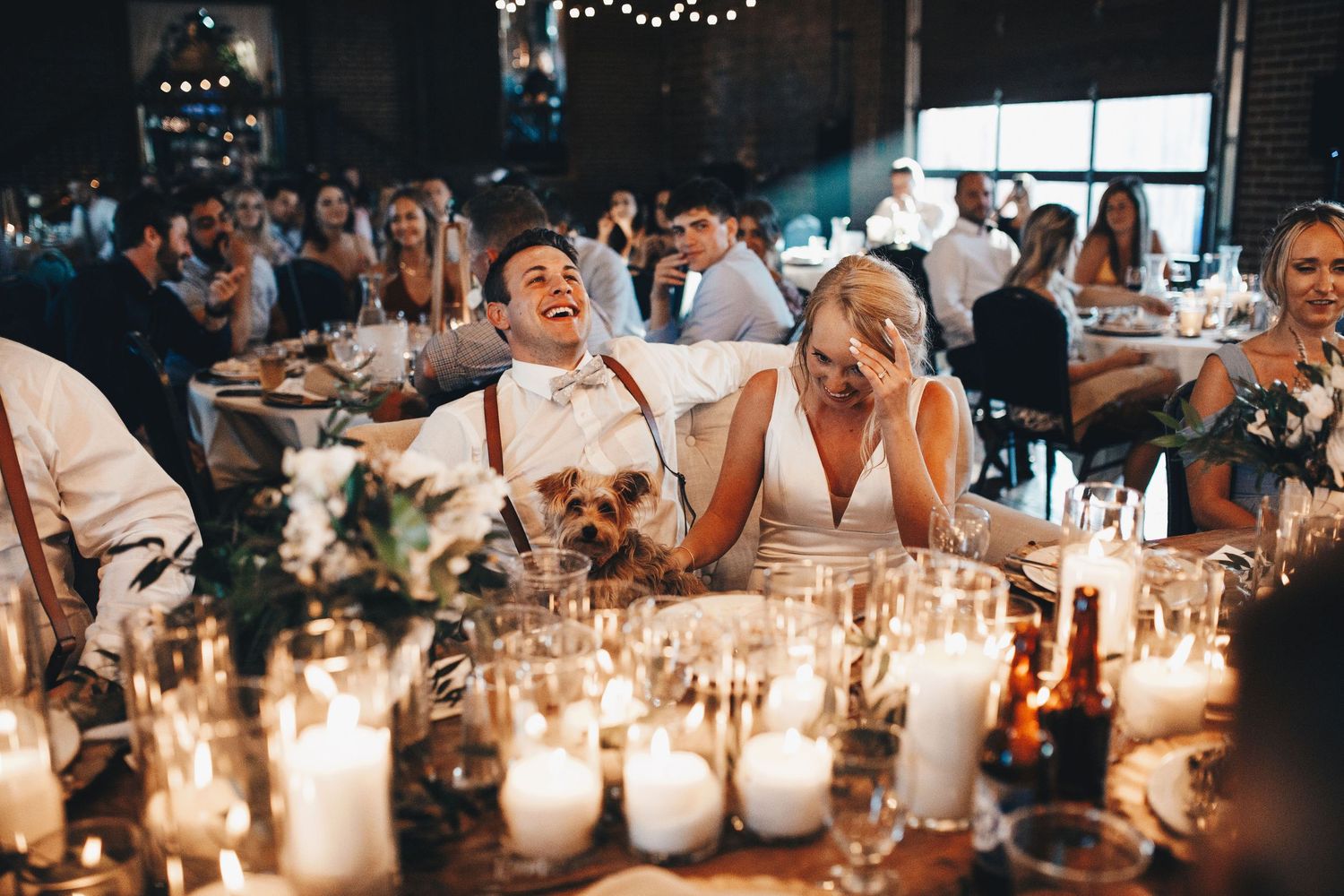 Bride and groom laugh joyfully at their candlelit wedding reception dinner table.