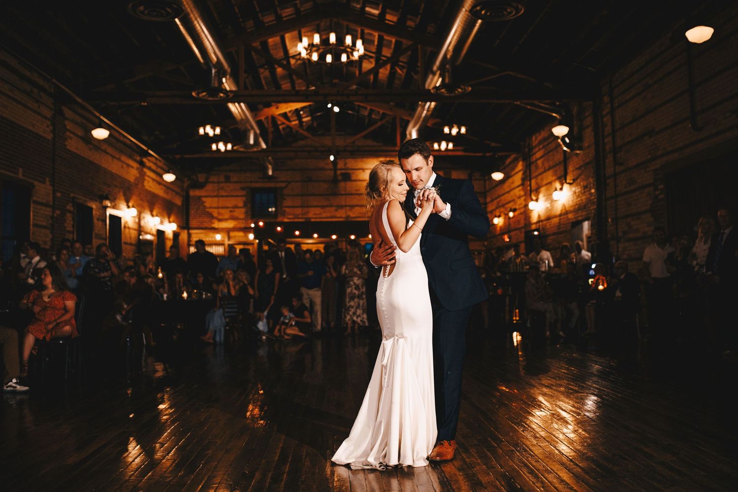 Bride and groom share their first dance in a rustic candlelit wedding venue.