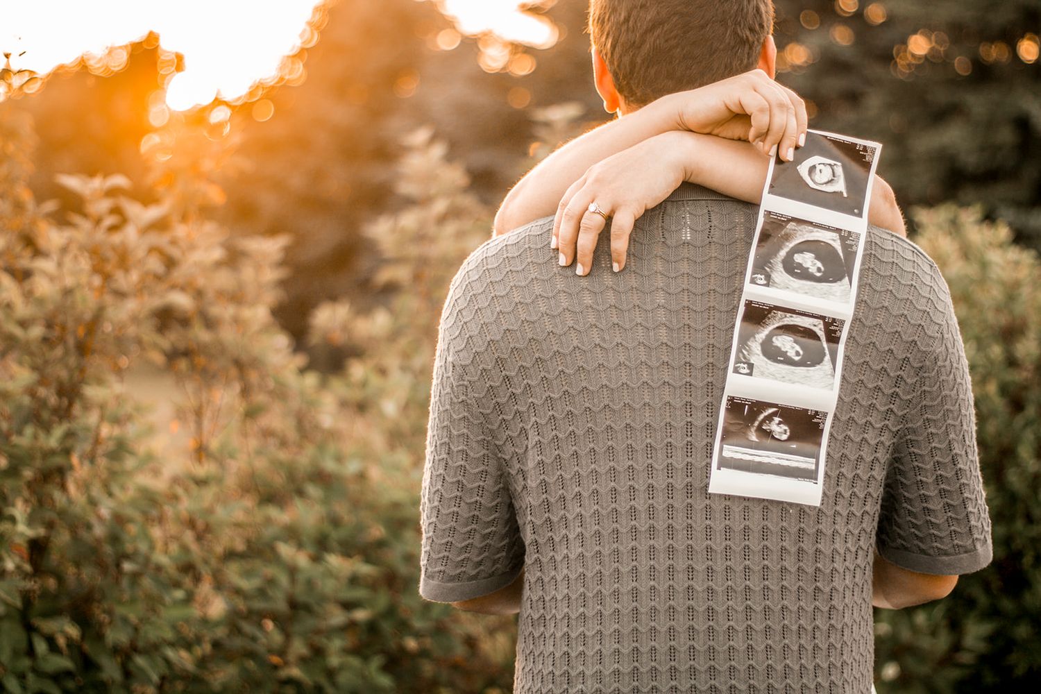 Man holding ultrasound photos behind his back during a pregnancy announcement shoot.
