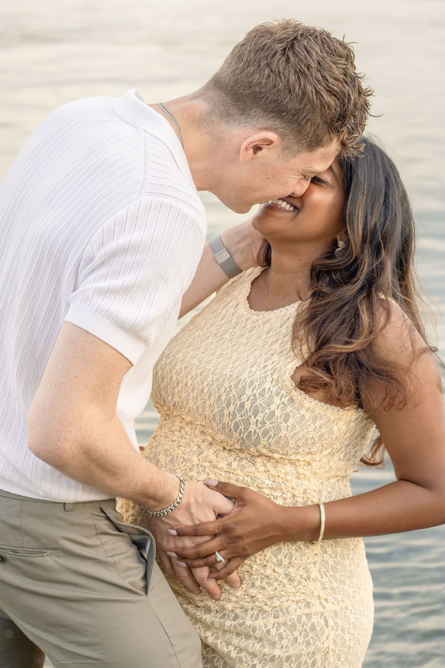 Séance photo grossesse en couple au bord de l’eau, un couple de futurs parents échange un tendre baiser.