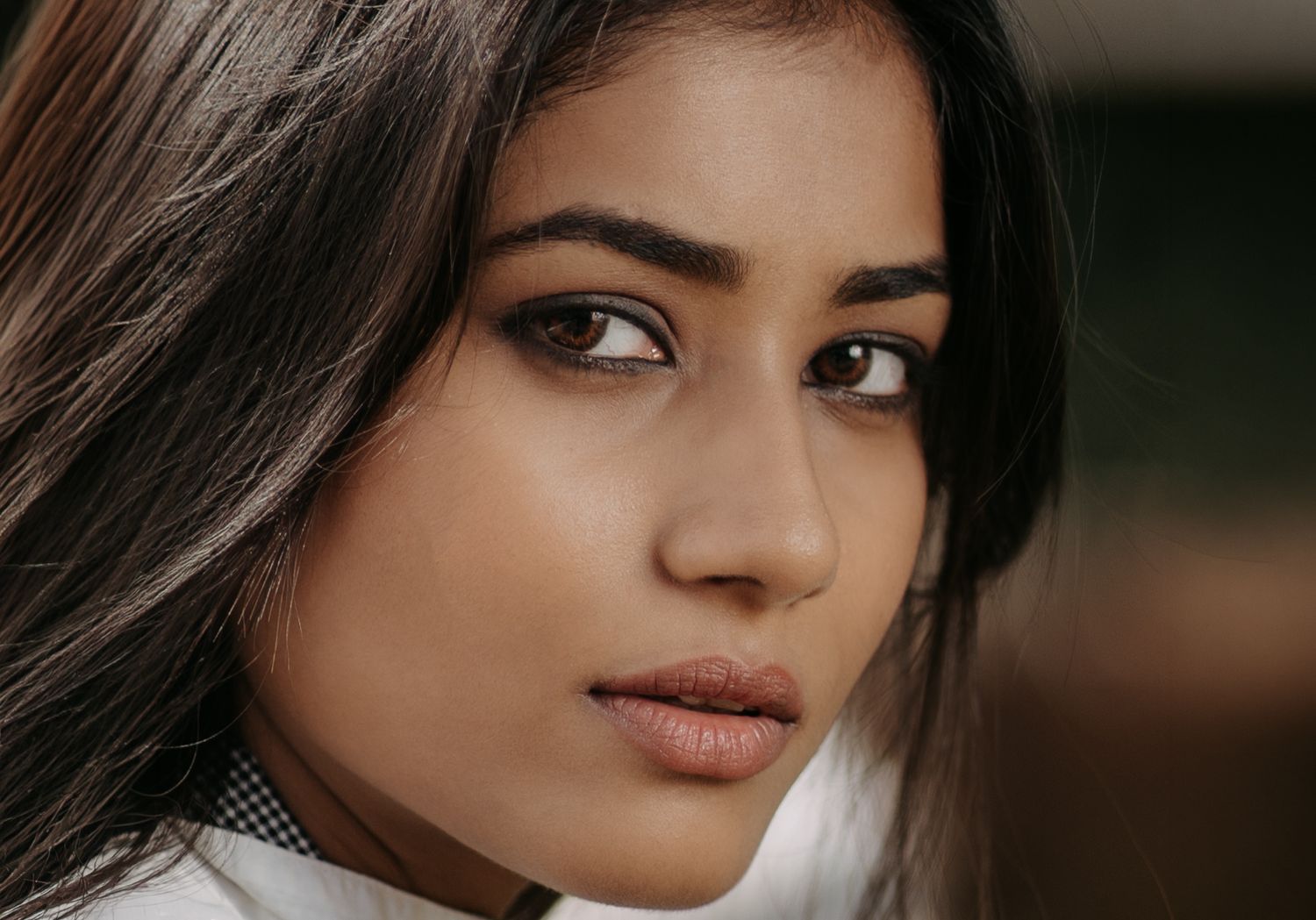Close-up portrait of a young South Asian woman with dark hair and brown eyes wearing natural makeup.