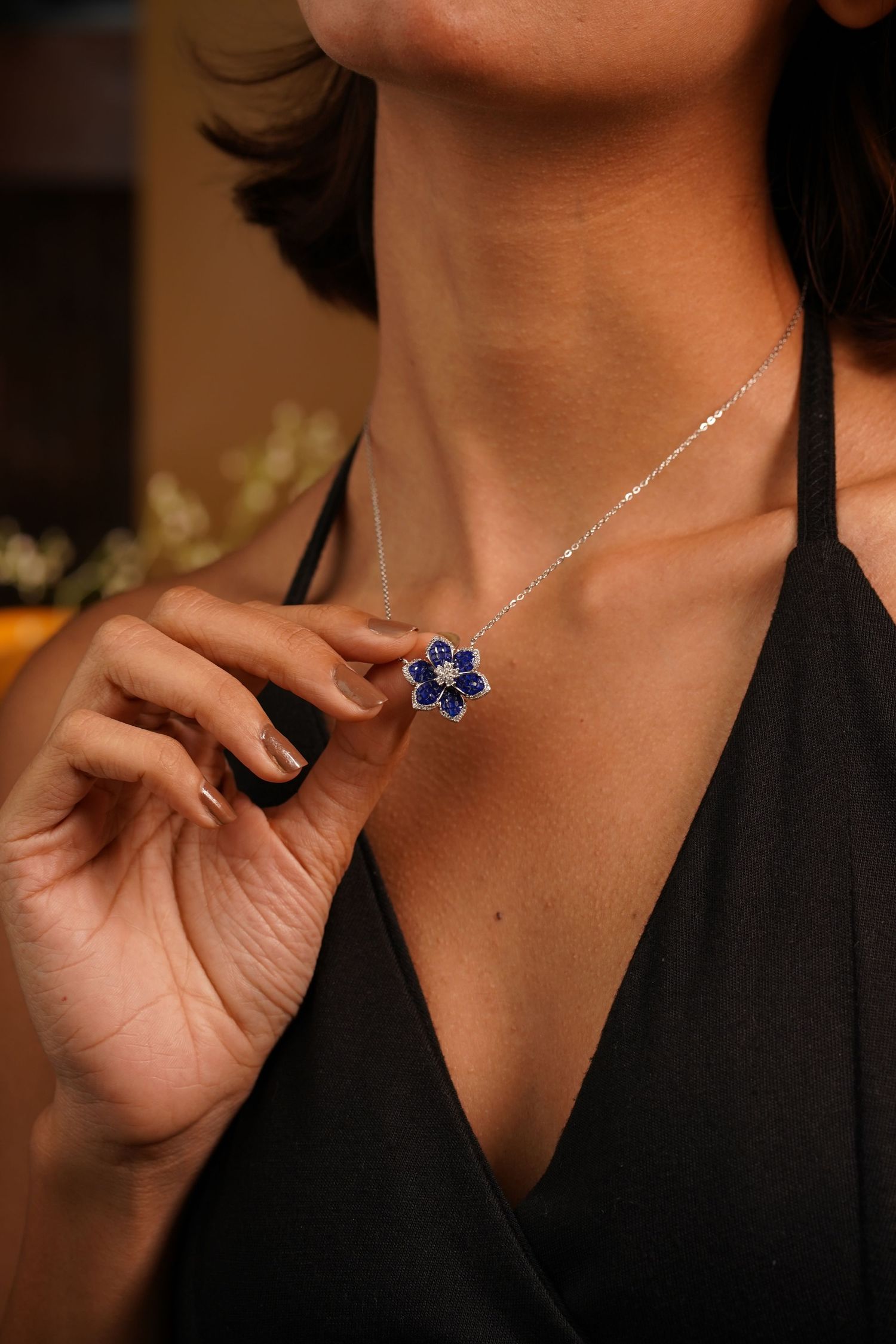 Woman wearing a silver chain necklace with a blue sapphire flower pendant, holding it gently against her chest.