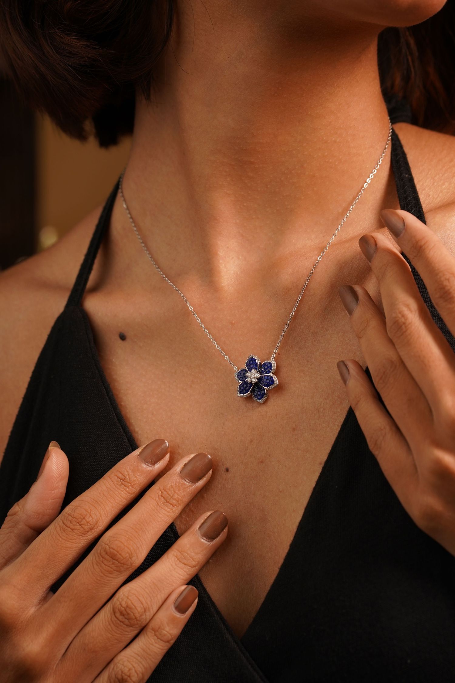 Woman wearing a silver flower pendant necklace with blue sapphire petals and diamond center on a delicate chain.