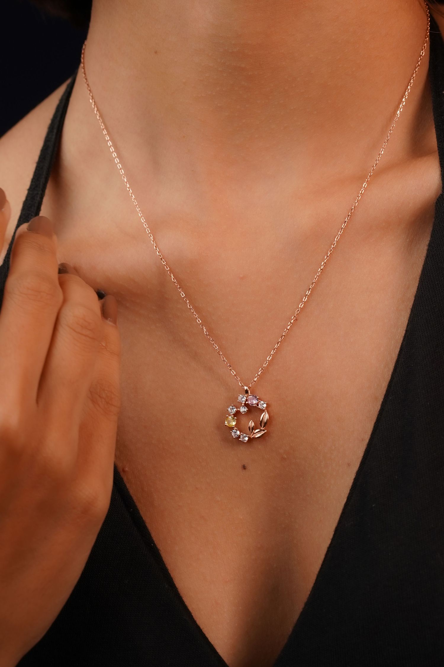 Rose gold chain necklace with floral crystal pendant worn by a model in a black top.