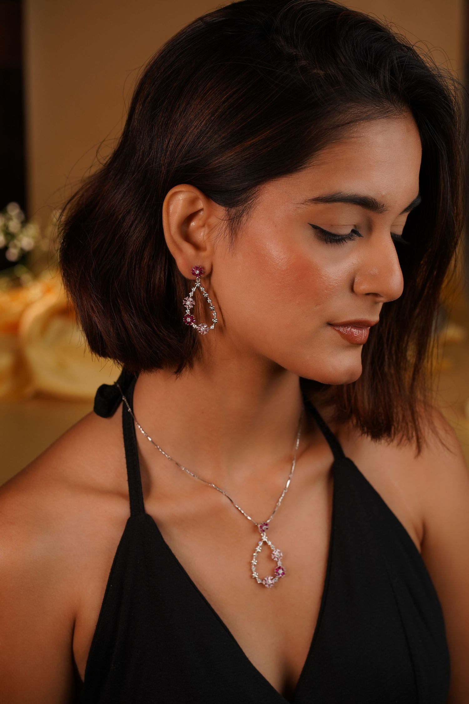 Woman wearing elegant teardrop pink gemstone earrings and matching necklace in silver setting, dressed in black halter top.