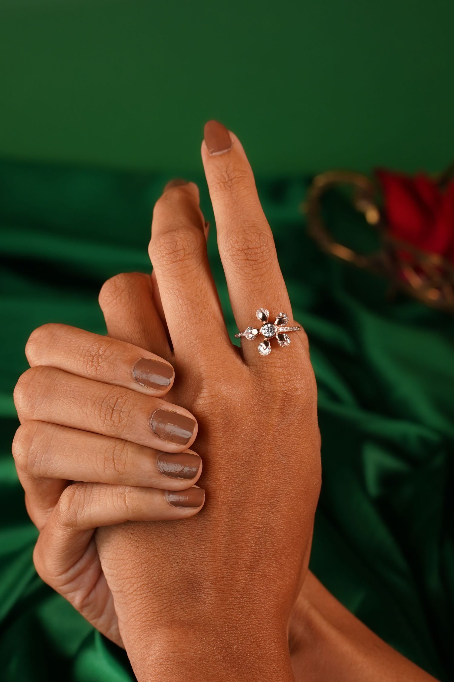 Close-up of a hand wearing an elegant floral diamond ring on index finger against a green silk background.