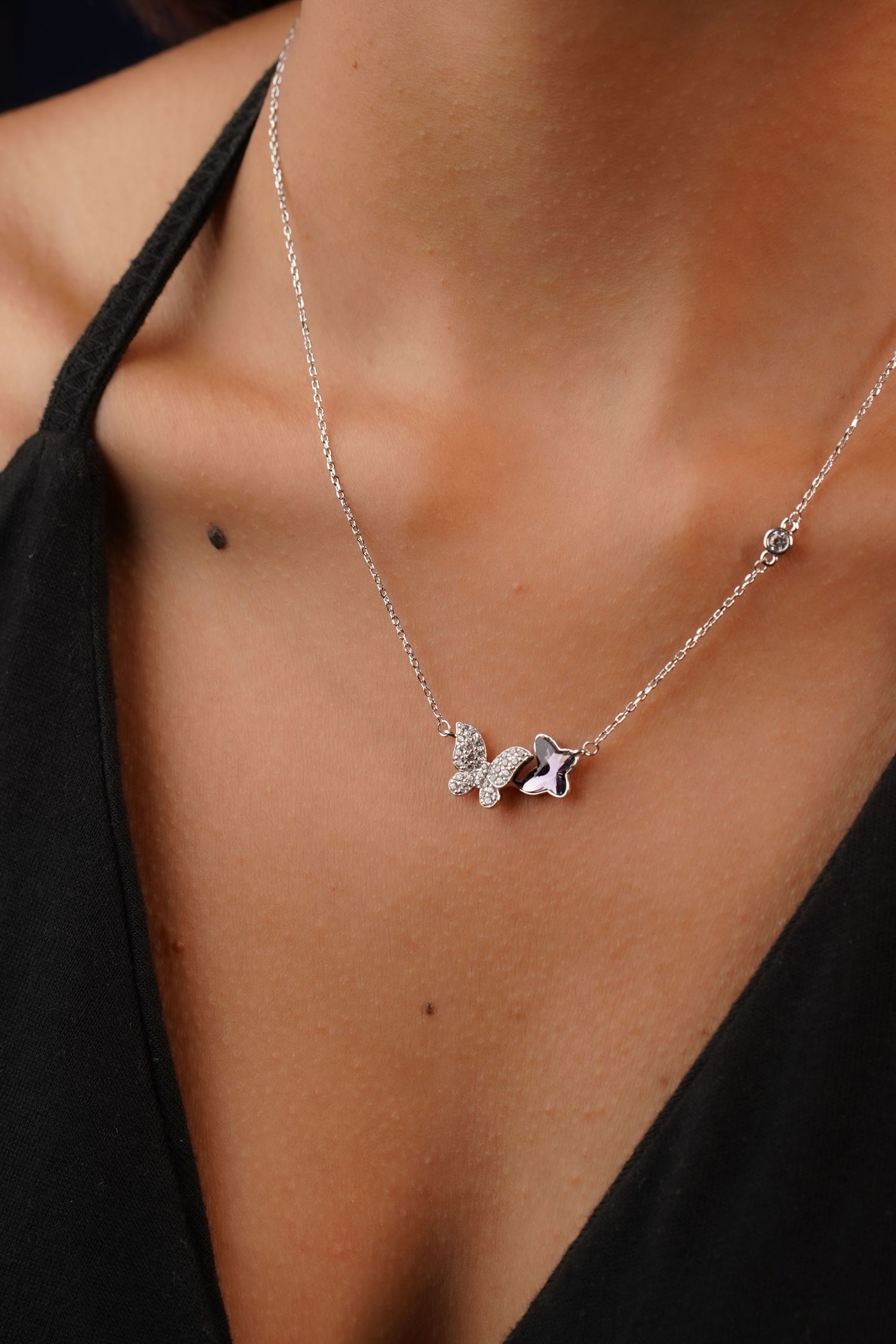 Silver chain necklace with crystal butterfly and star pendants worn by a woman in a black top.