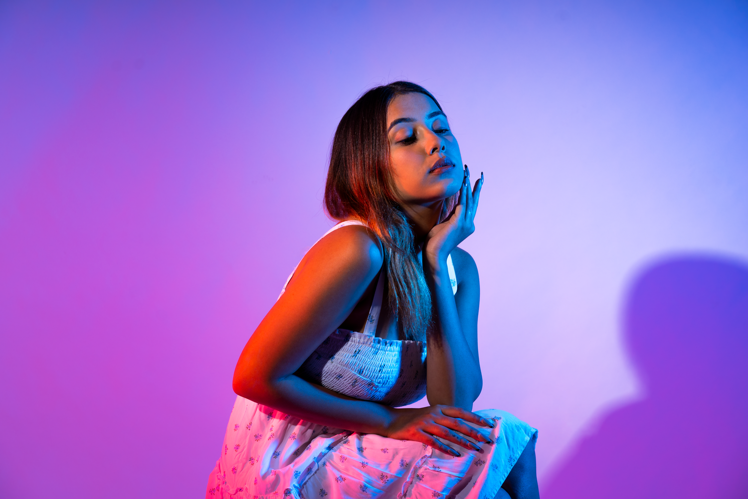 Young woman in floral dress poses gracefully under vibrant blue and pink studio lighting.