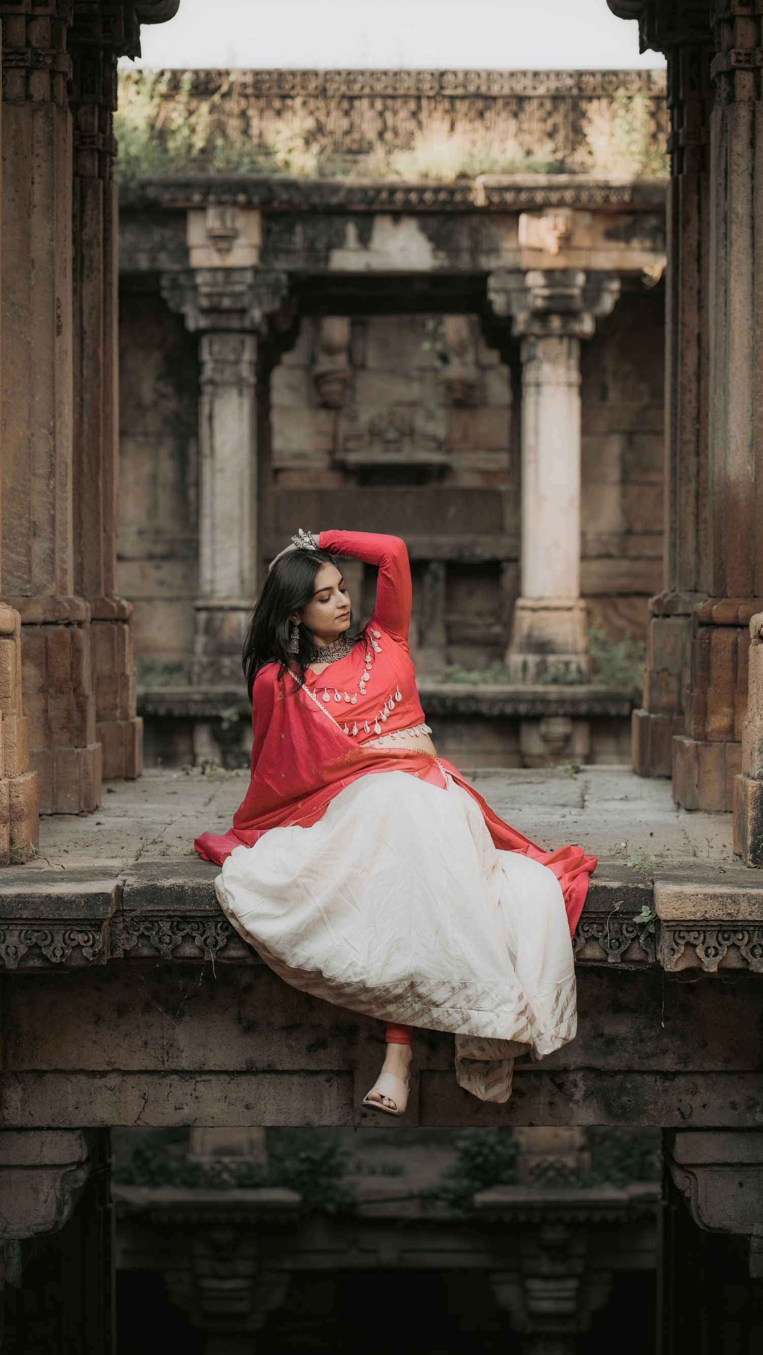 Woman in red and white traditional Indian attire poses gracefully at an ancient stone temple.