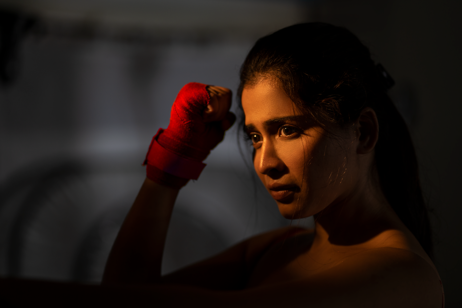 Female boxer with red hand wraps raised in fighting stance, dramatic low-key lighting highlighting her focused expression.