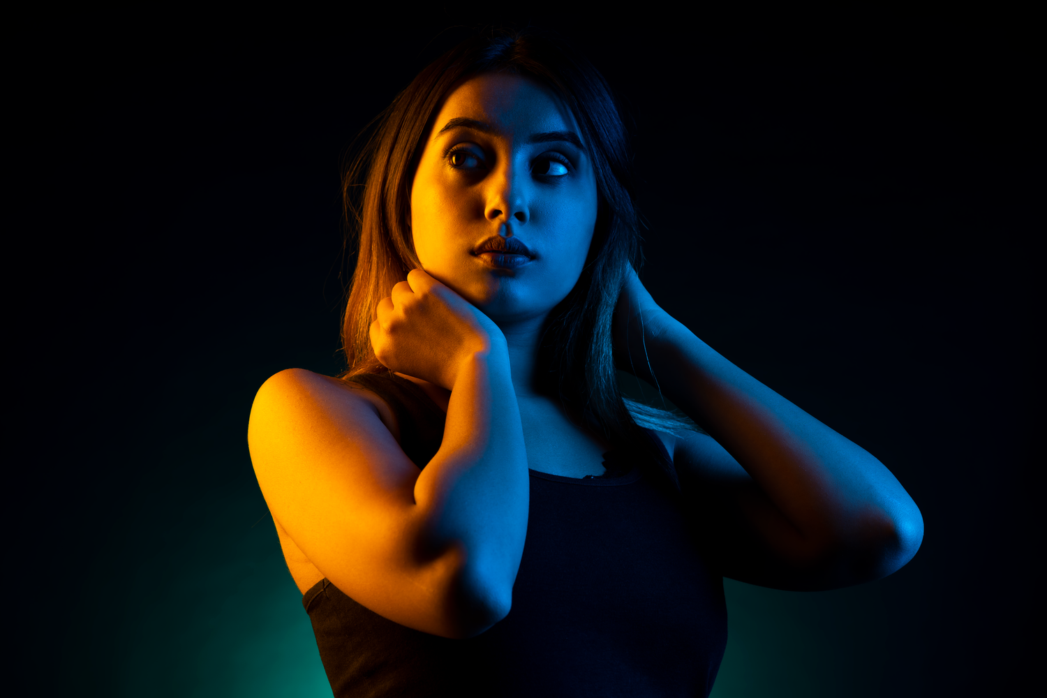 Young woman posing dramatically under colorful neon blue and orange studio lighting against dark background.