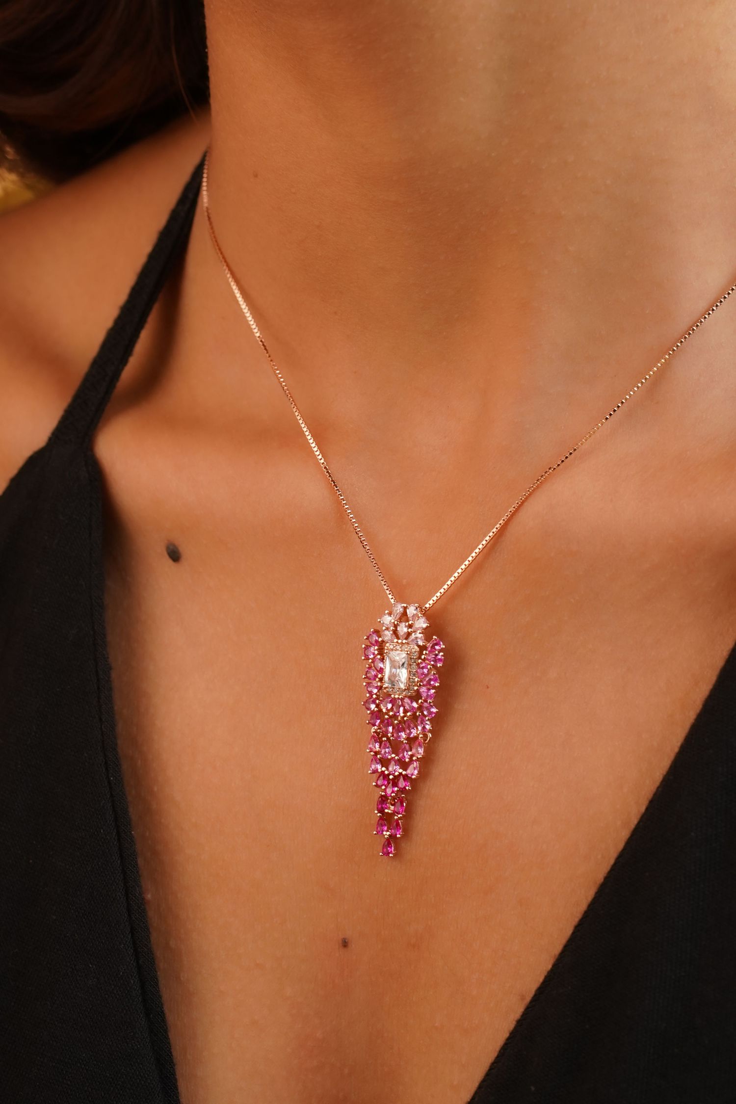 Rose gold necklace with pink gemstone drop pendant worn by a model in a black top.