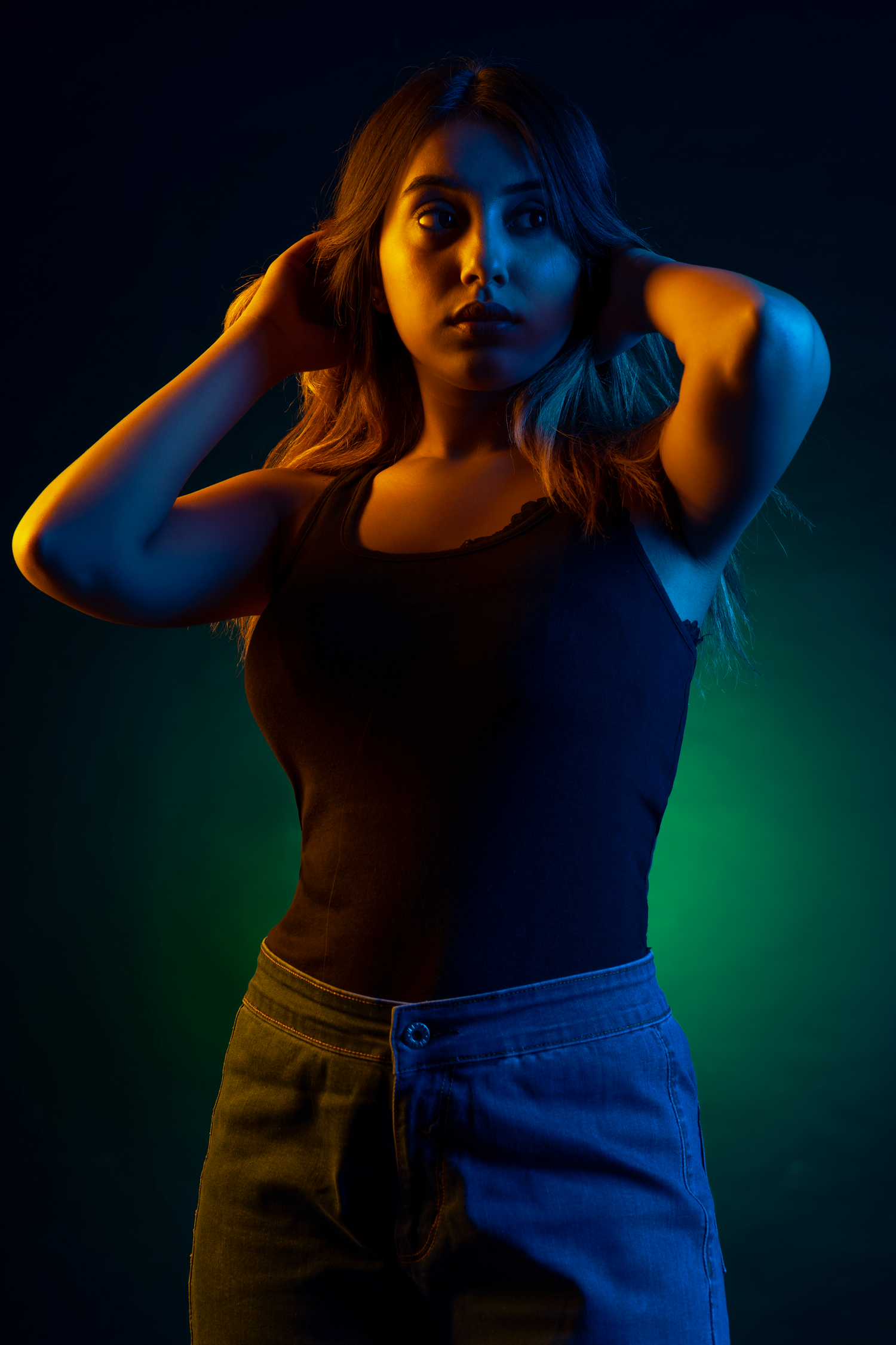 Woman posing dramatically under colorful neon lights in blue and orange tones against a dark background.