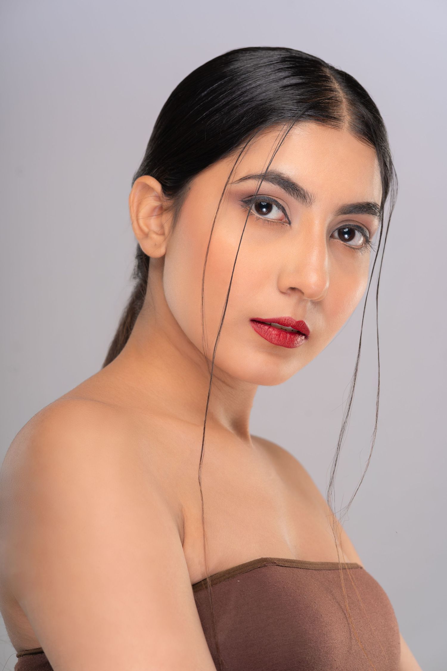 Young Asian woman with red lips, sleek black hair, and bare shoulders poses against a gray background.