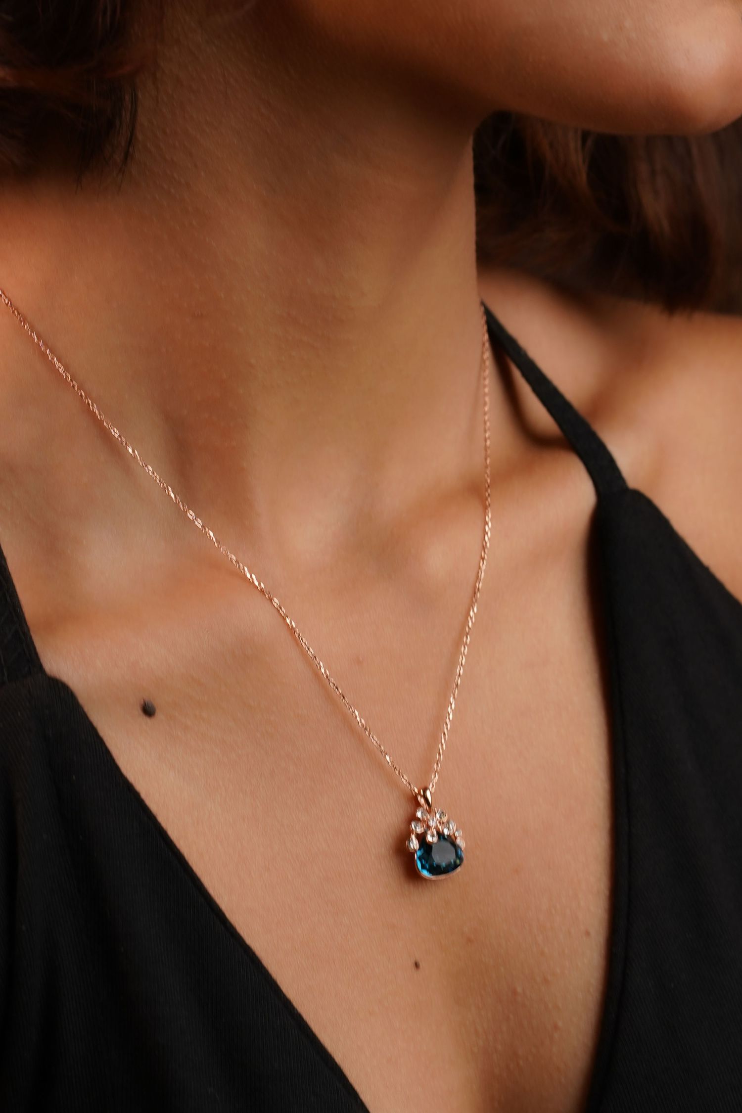 Rose gold chain necklace with a blue gemstone pendant worn by a woman in a black top.