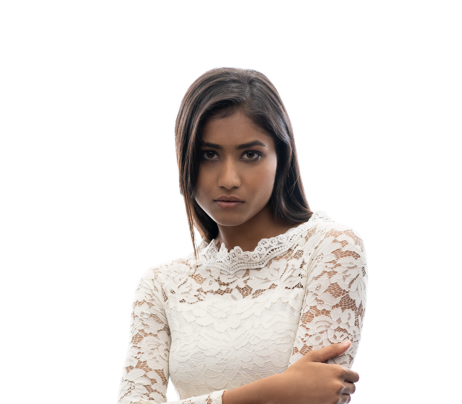 Young woman in white lace dress with arms crossed, looking serious against a white background.