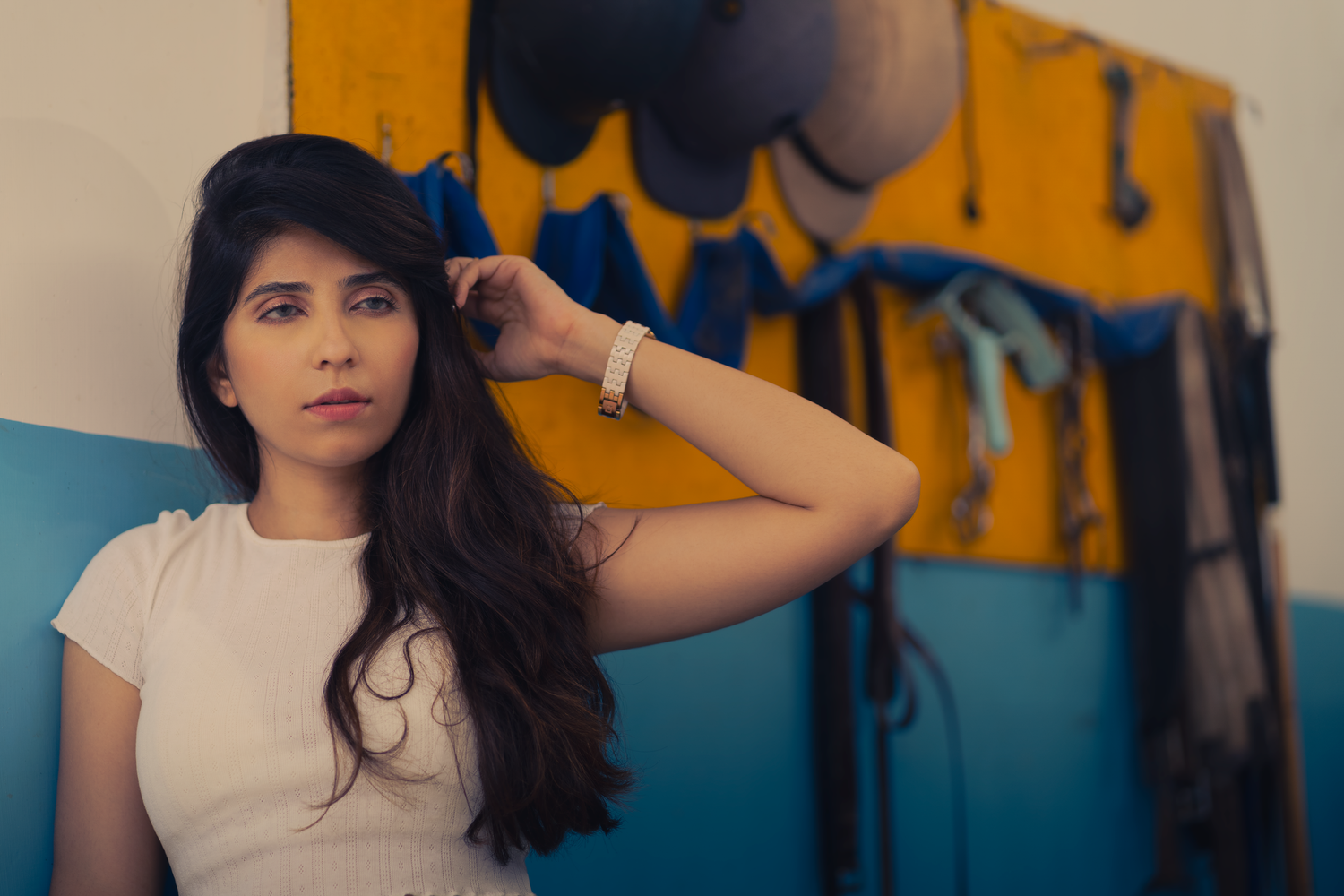 Young woman with long dark hair in white top poses against colorful blue and yellow wall art.