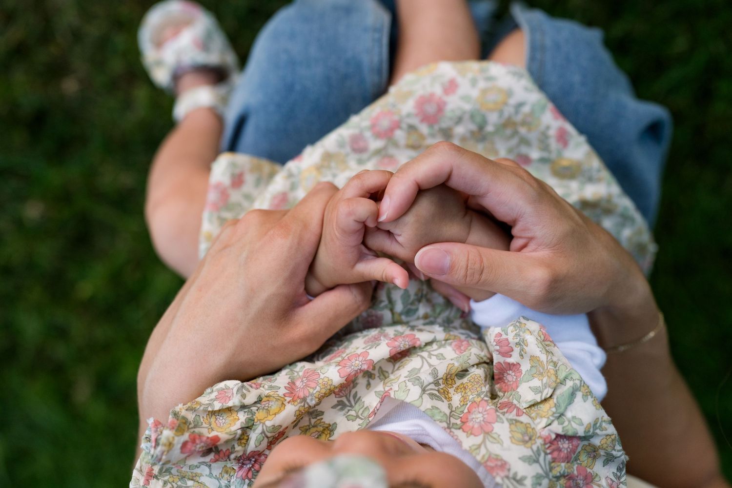 Close-up of mother and baby holding hands in matching floral outfits outdoors.