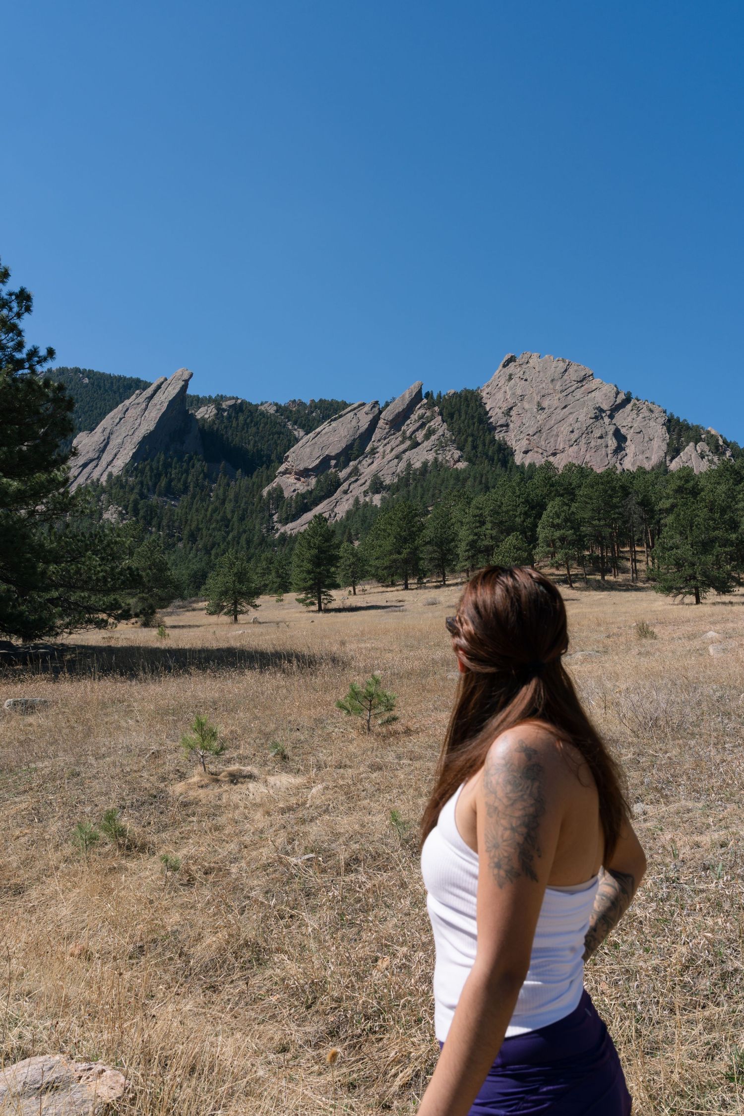 Woman with long hair and tattoo views the iconic Boulder Flatirons rock formations in Colorado.