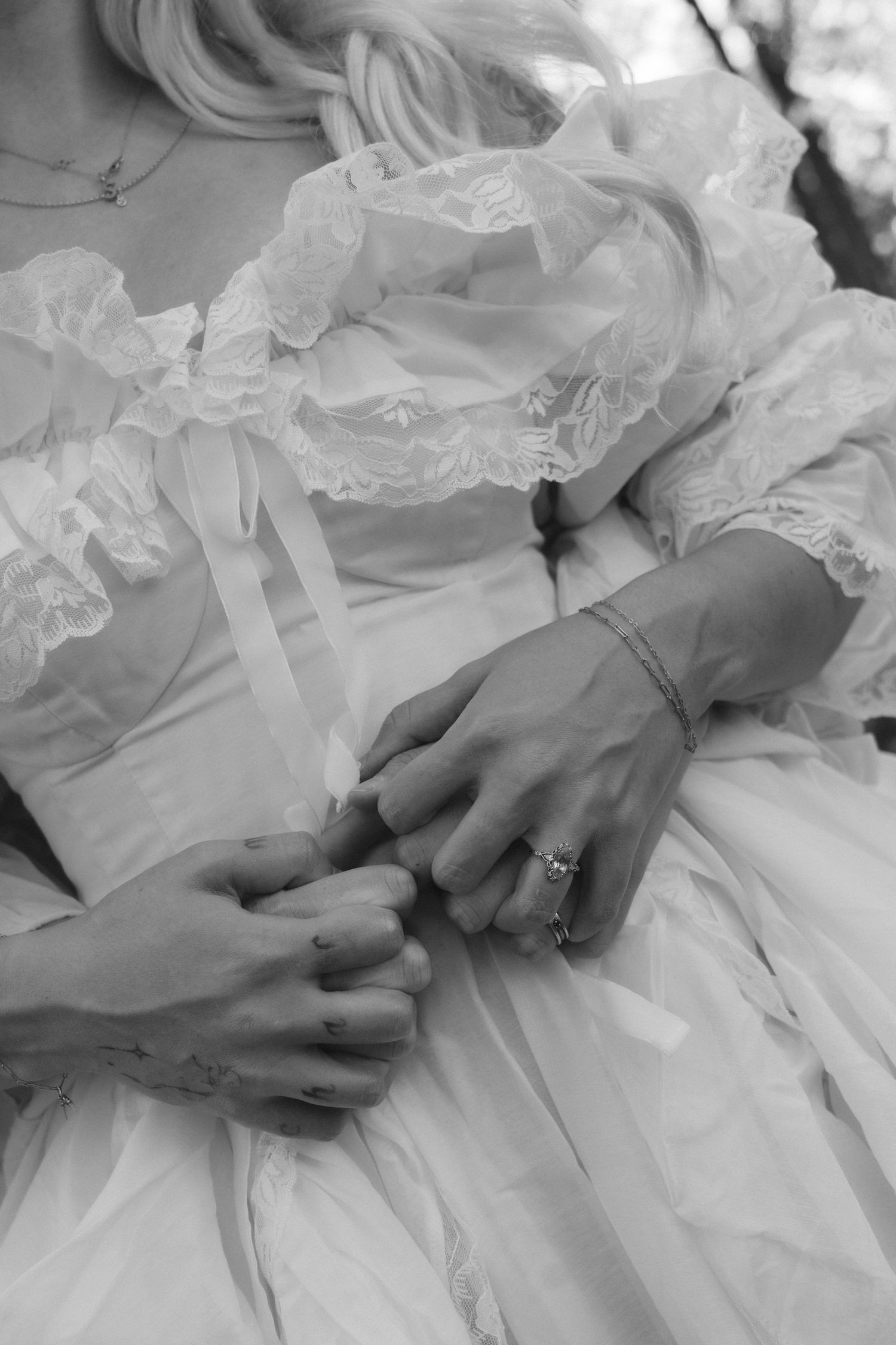 Black and white photo of a bride in a ruffled wedding gown, hands clasped together wearing a diamond ring and bracelet.