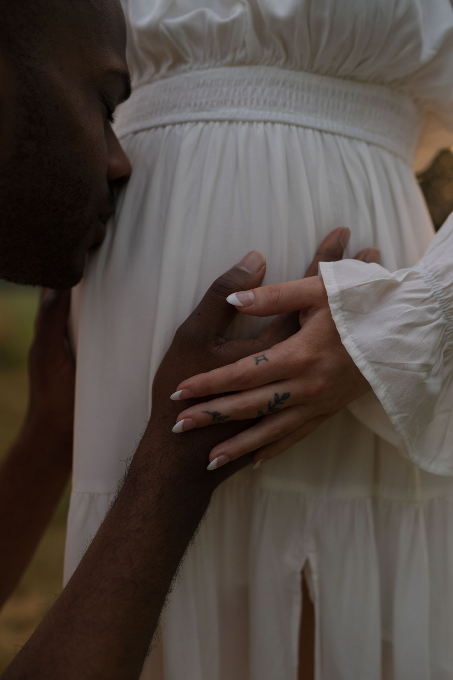 Expectant parents standing together in the tall prairie grasses at sunset.